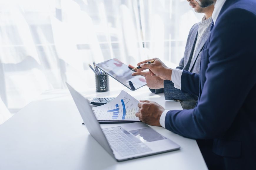 Two businesspeople reviewing documents beside a laptop in a bright office