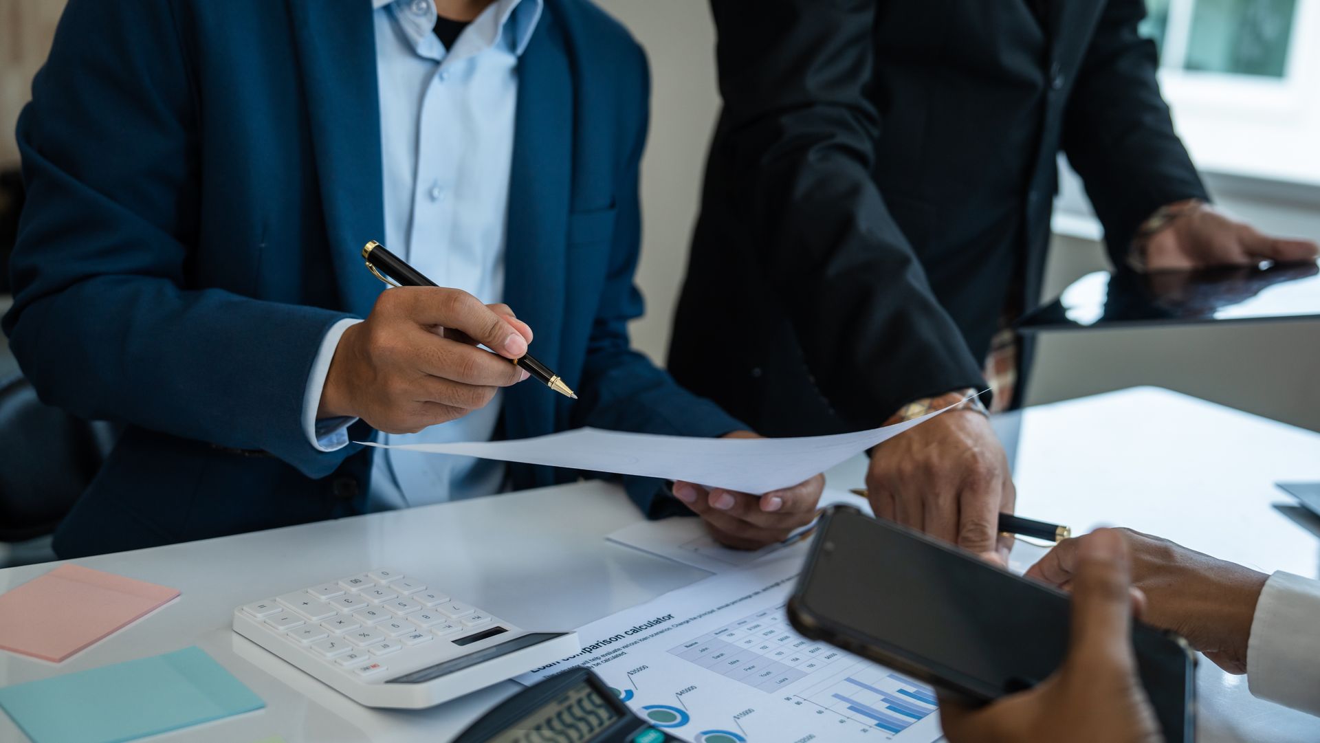 People reviewing documents at a table with a tablet, calculator, and charts.