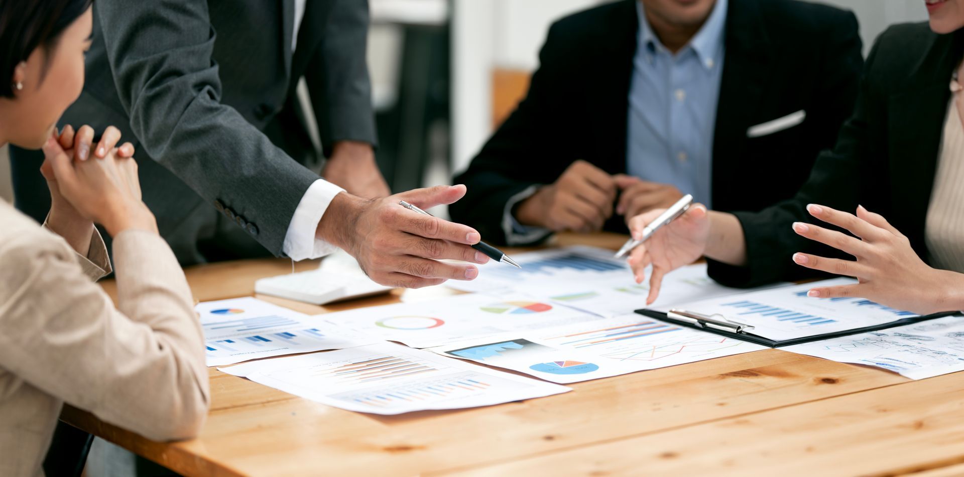 Business meeting with people in suits discussing charts spread across a wooden table