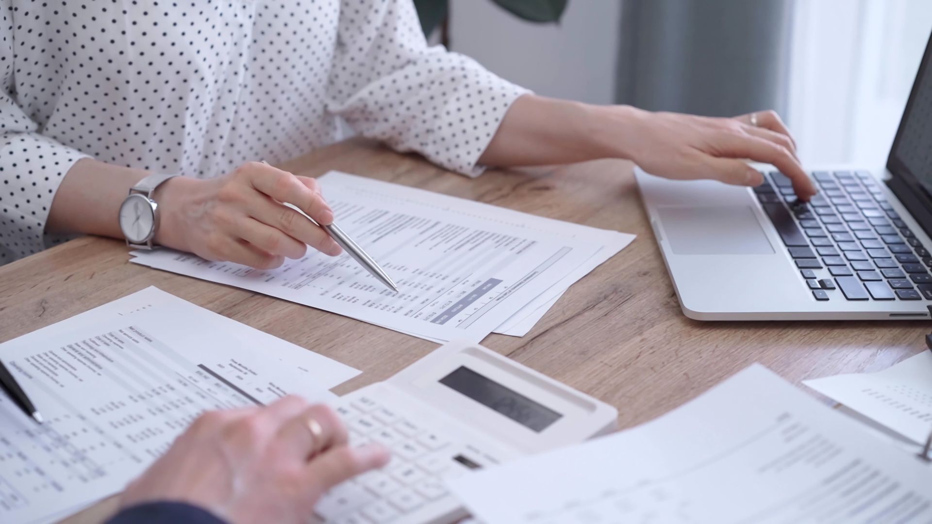 Hands reviewing printed documents beside a laptop on a desk.