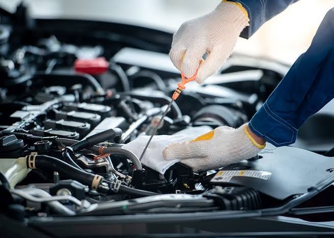 Gloved hands using a dipstick to check a car engine in an open hood bay