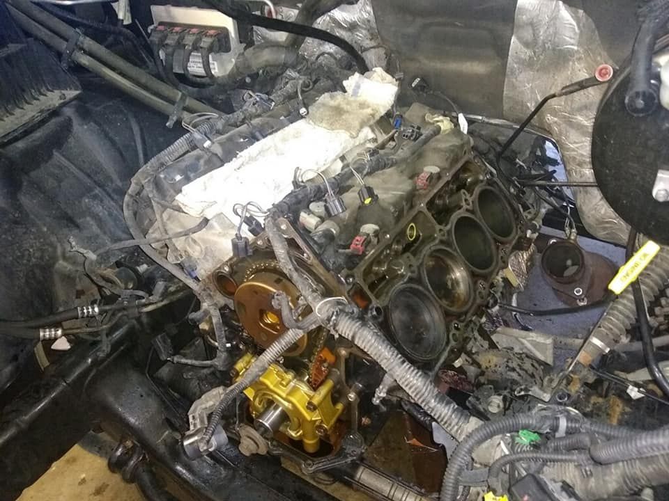 An open V8 car engine block with exposed cylinders and removed head components in a vehicle engine bay.