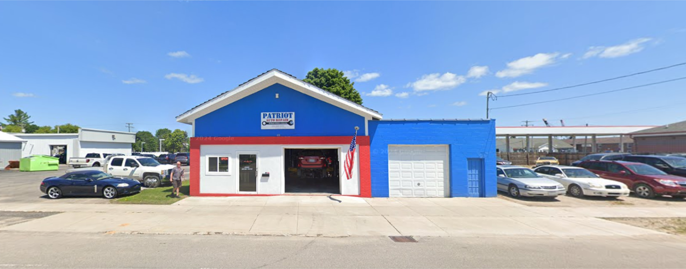 Blue auto shop with red-trimmed entrance, white garage door, and parked cars under a sunny sky