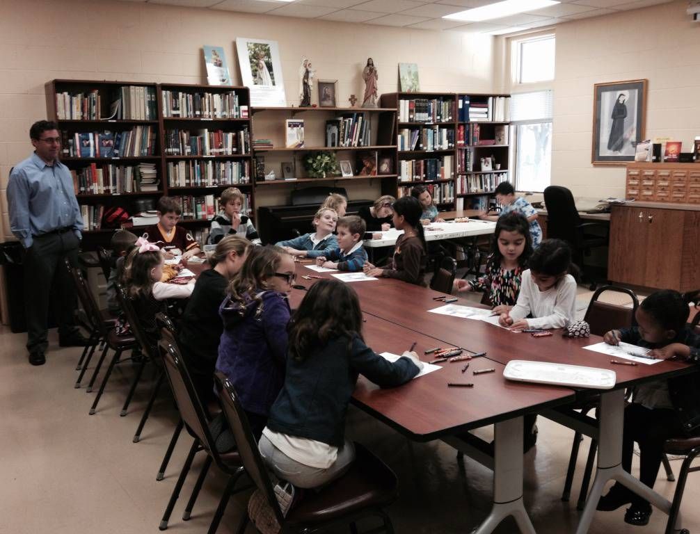 Library classroom with children seated around tables and a teacher standing nearby