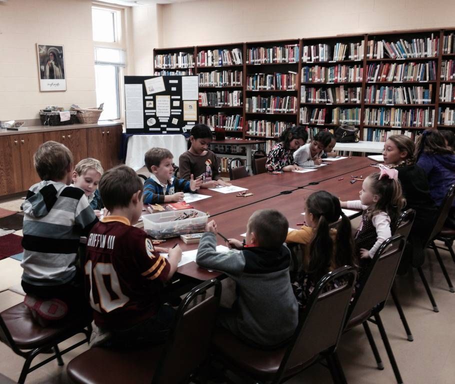 Children gathered around a long table in a library, reading and working together.