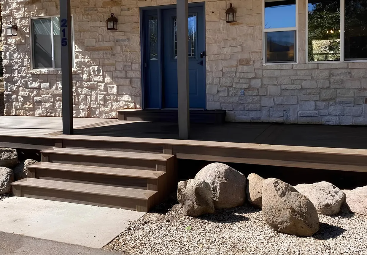 Stone-walled house with blue front doors, porch with steps, and large rocks in the front yard.