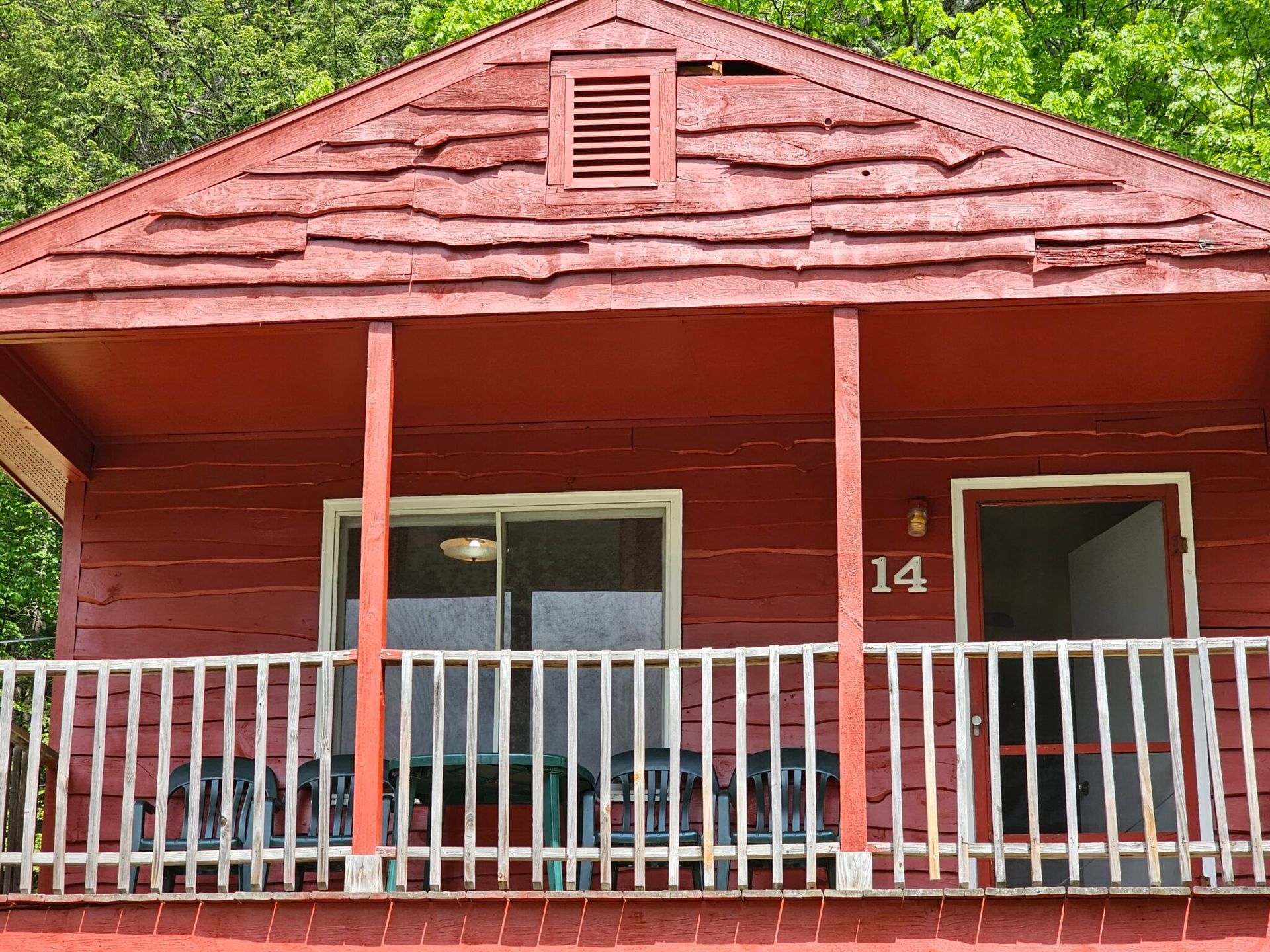 Red wooden cabin porch with white railing and two chairs, number 14 on the door.
