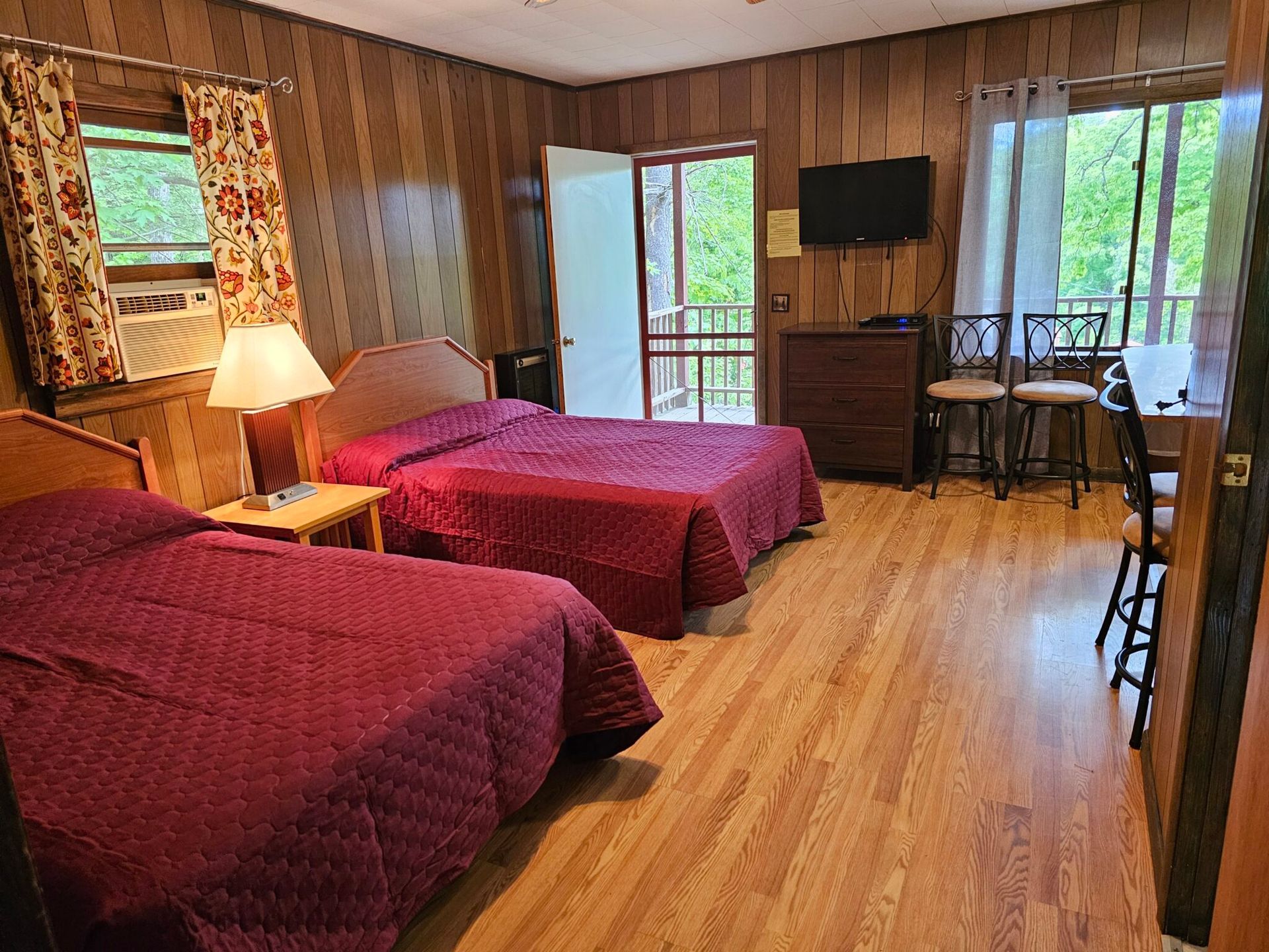 Hotel room with two red beds, wood paneling, and a desk by the window.