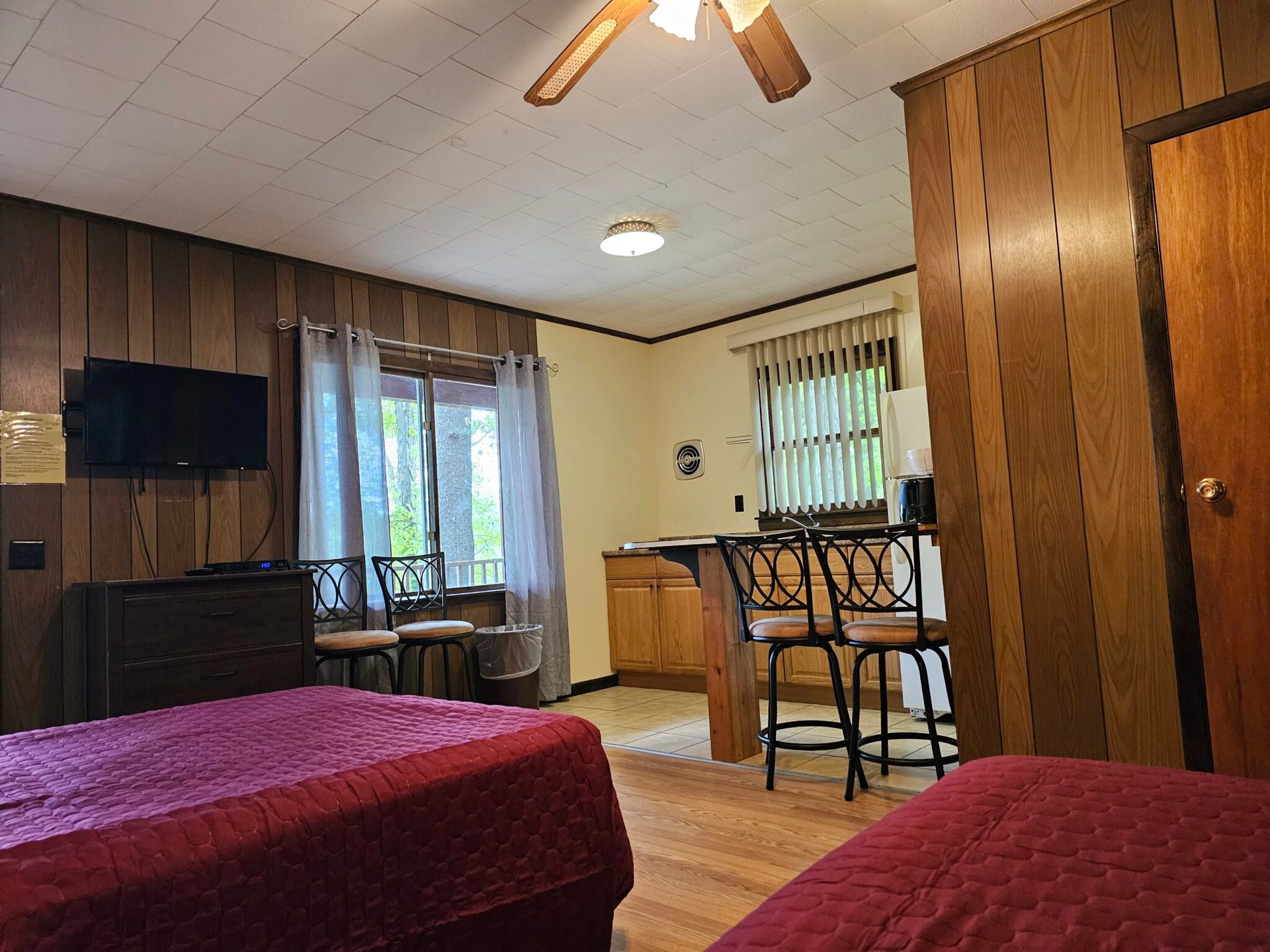 Motel room with two beds, wood-paneled walls, TV, windows, and a small table and chairs