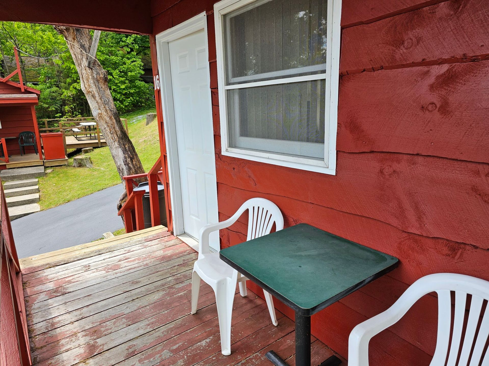 Small red porch with white chairs, green table, and white door beside steps and a grassy yard