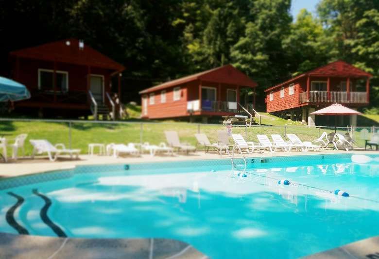 Outdoor pool with lounge chairs and red cabins on a grassy hillside