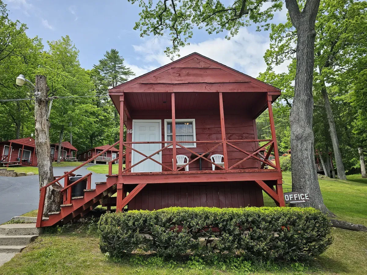 Red cabin porch with chairs, stairs, and red railings among green trees and shrubs.