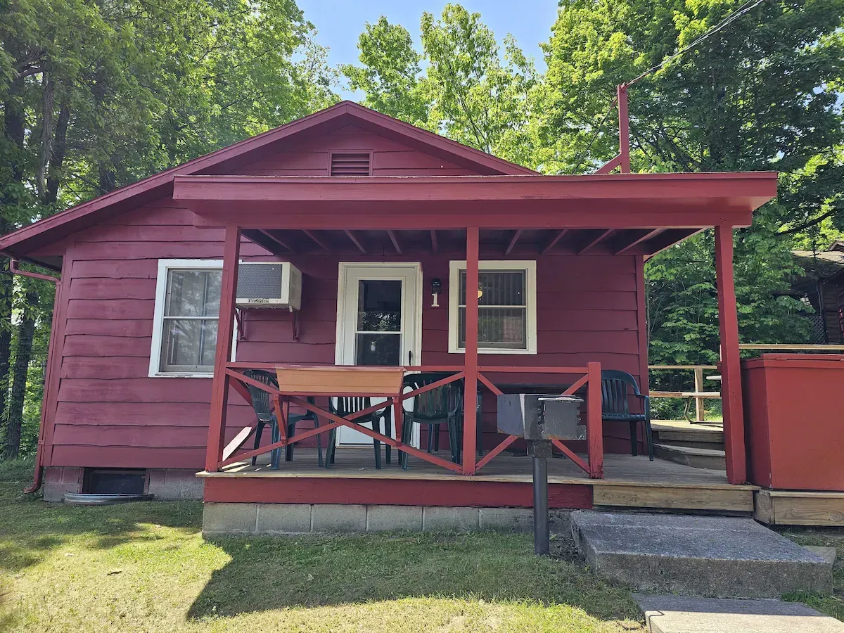Red cabin with a front porch and rocking chairs, surrounded by trees on a sunny day