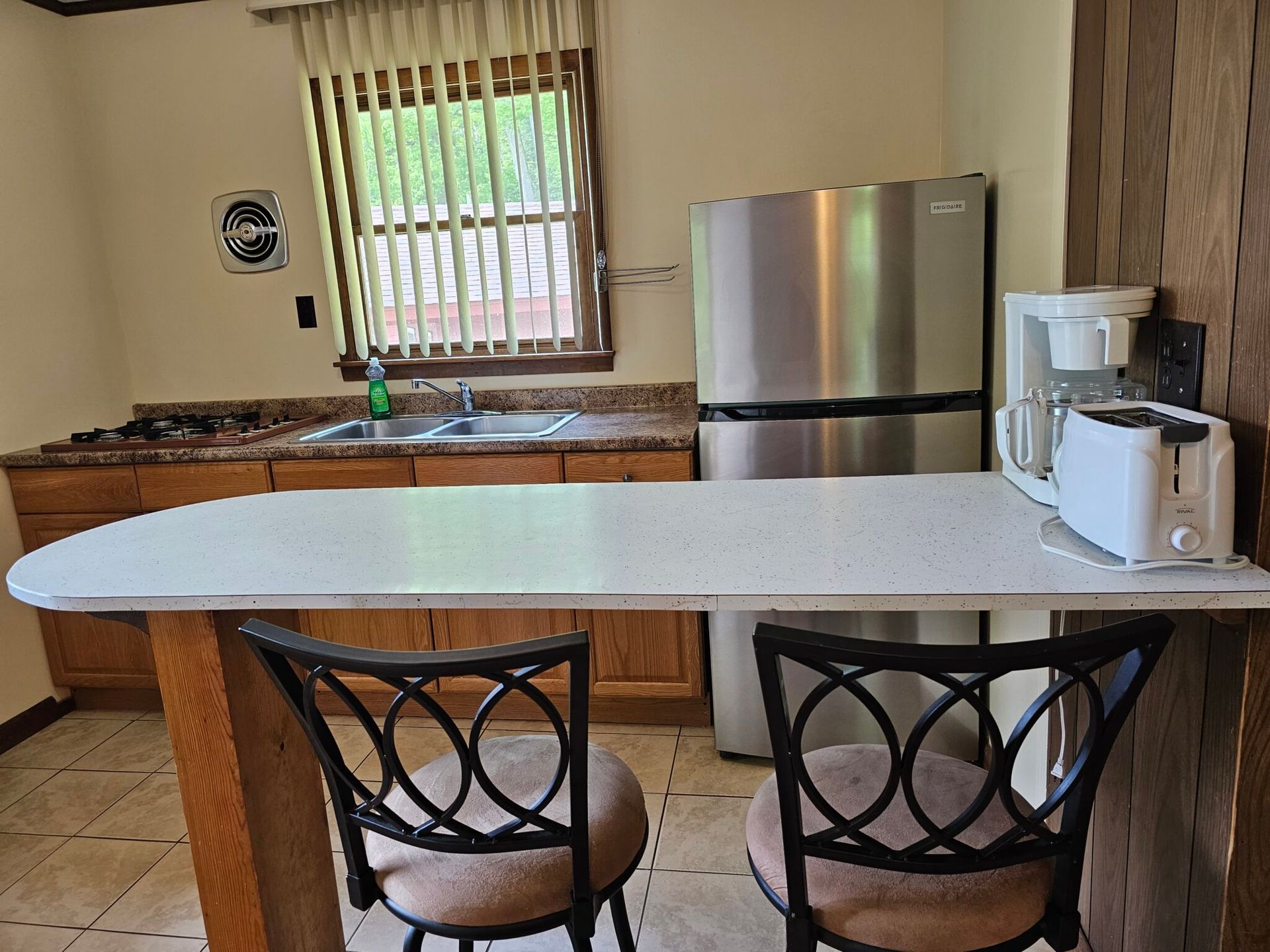 Kitchen with granite counter, stainless fridge, coffee maker, and white island table with two black chairs