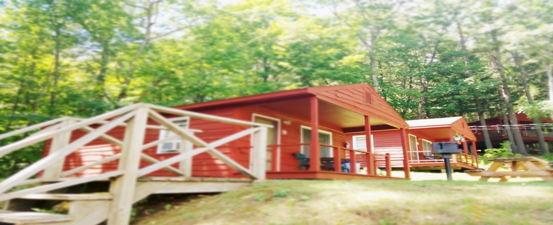 Red cabin with white railings on a wooded hillside, with a deck and picnic table in front.
