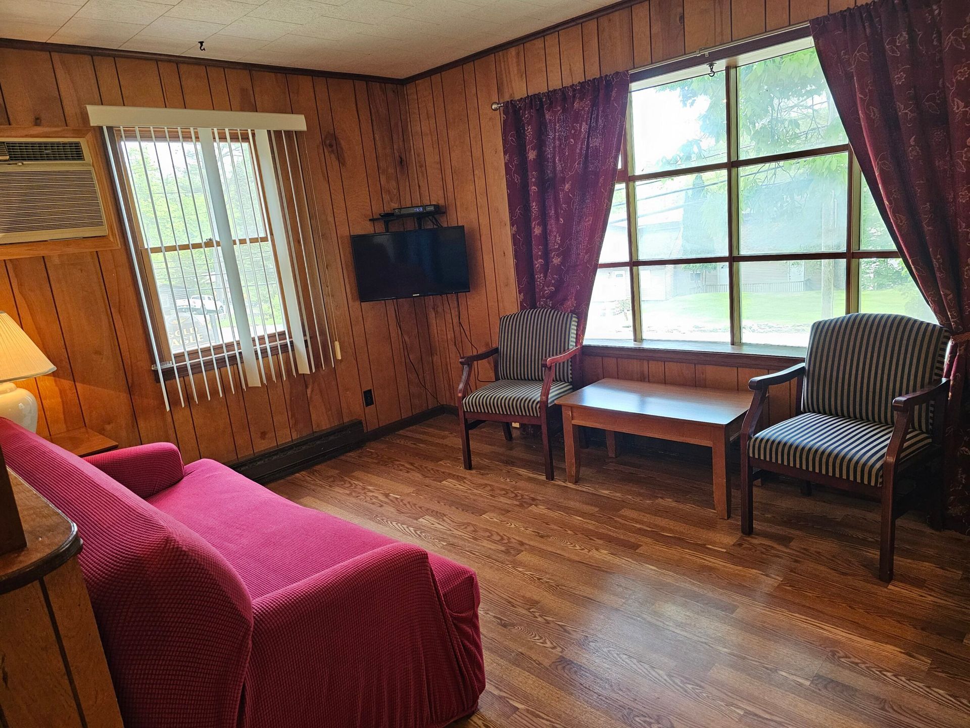 Cozy living room with pink sofa, two chairs, a wooden table, and large window with purple curtains