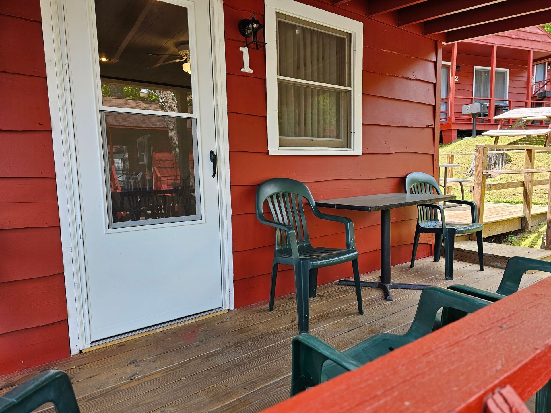 Red-painted porch with white door, small black table, green chairs, and wooden deck railing