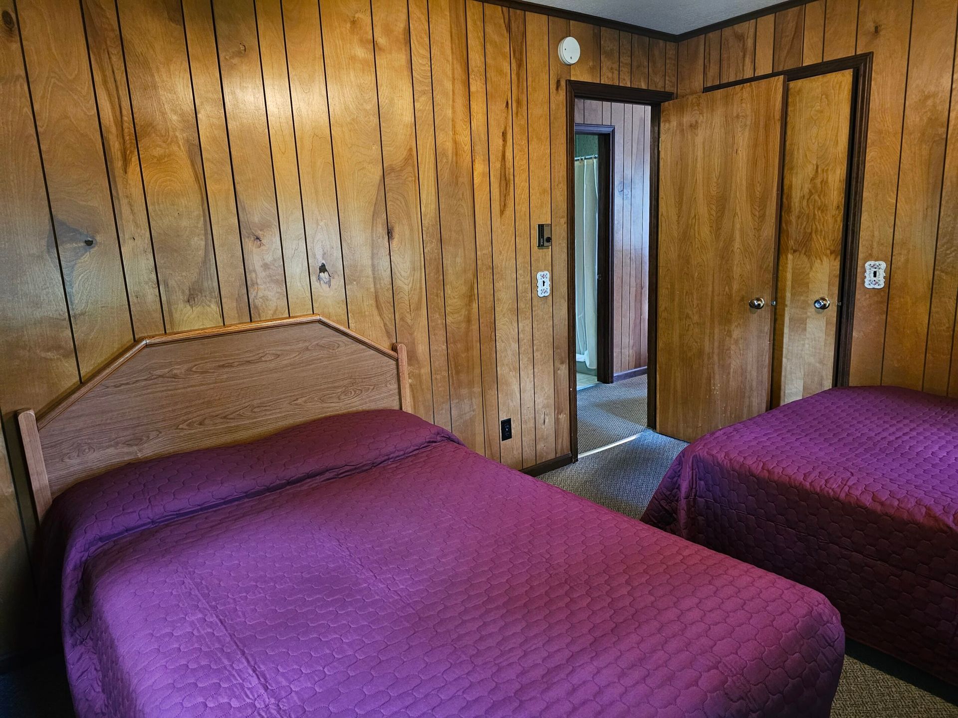 Wood-paneled bedroom with two purple-covered beds and an open doorway