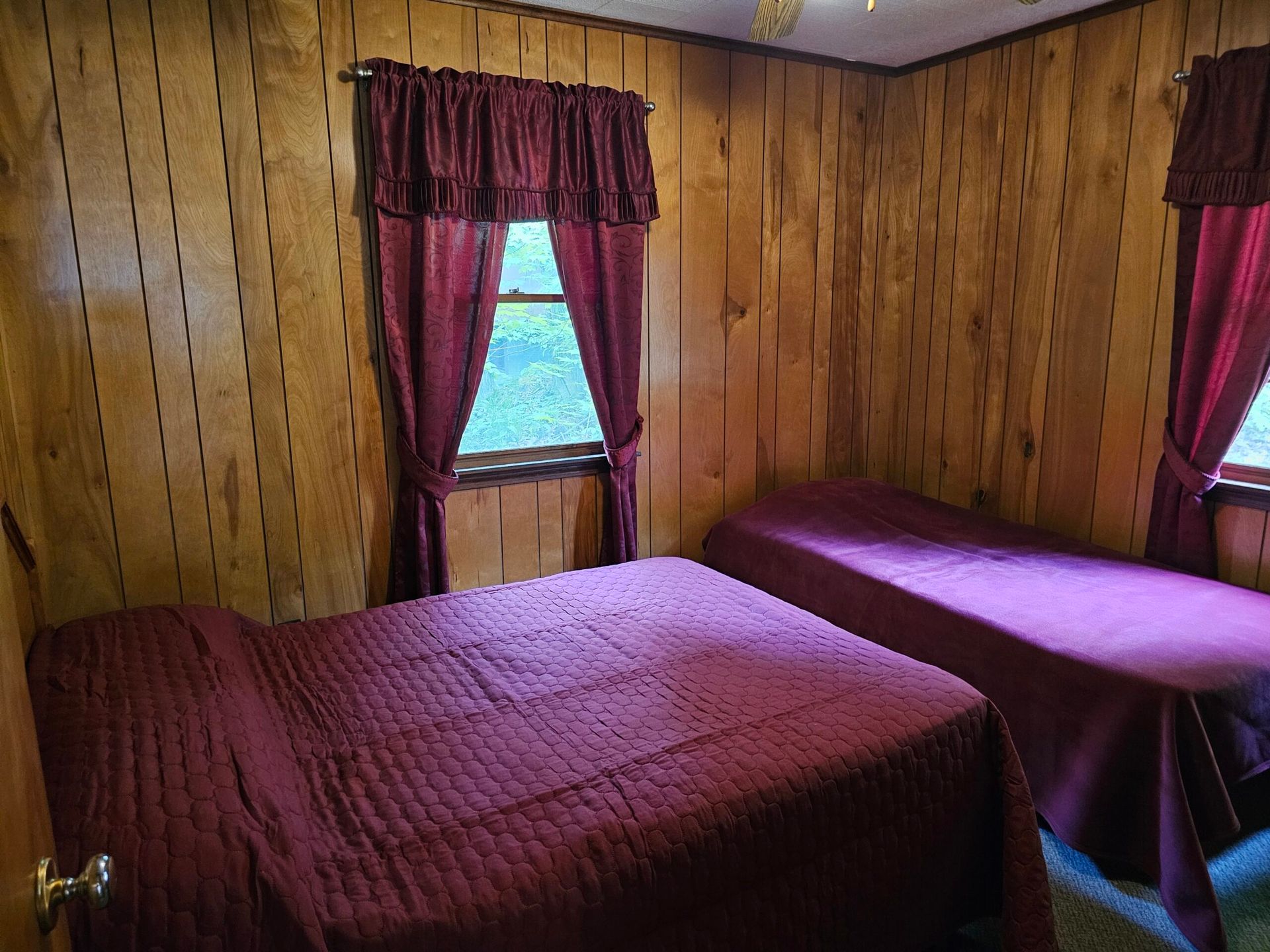 Small wood-paneled bedroom with two beds and purple curtains by the windows