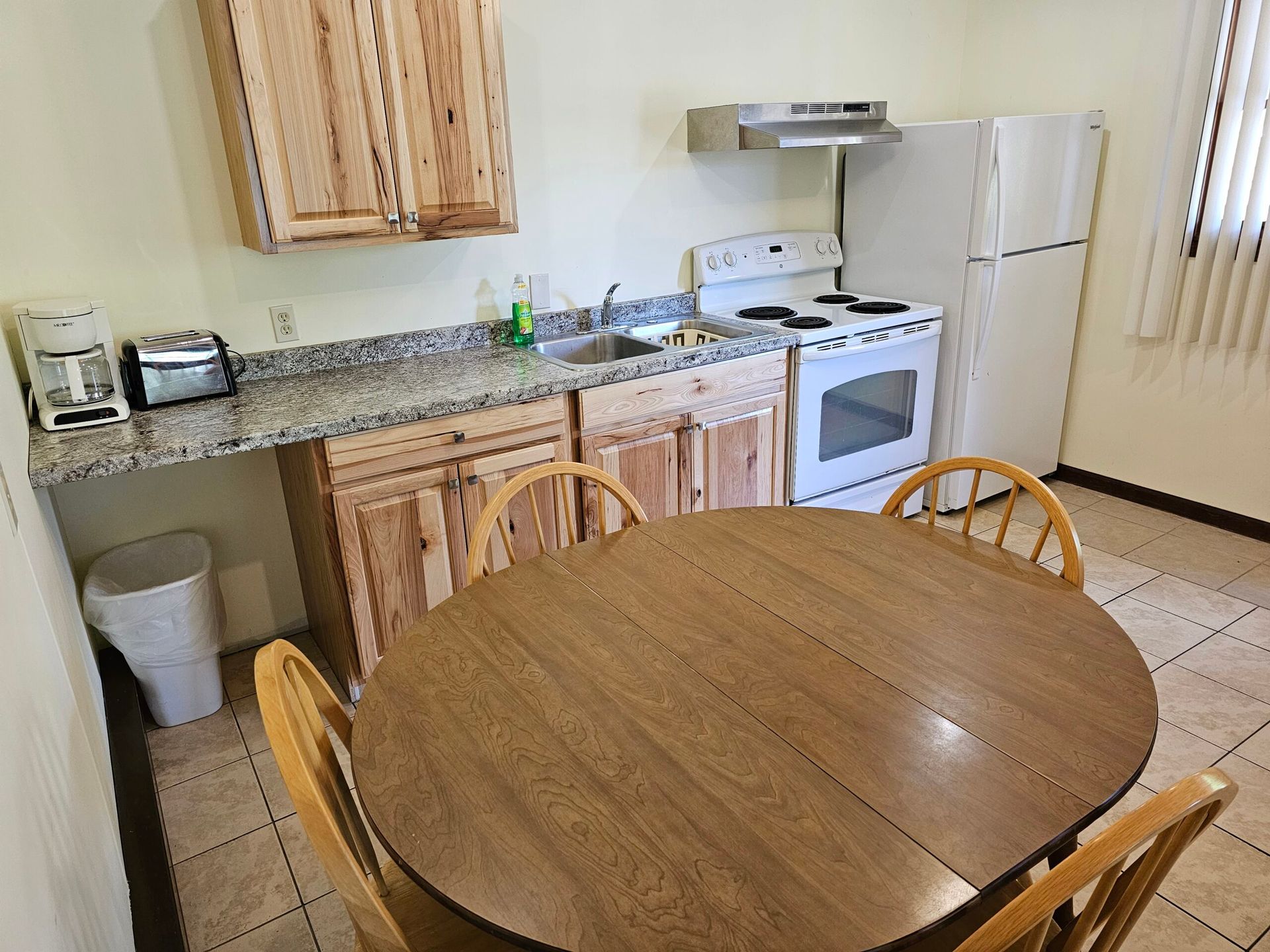 Small kitchen with wooden table, granite countertop, stove, fridge, and cabinets.