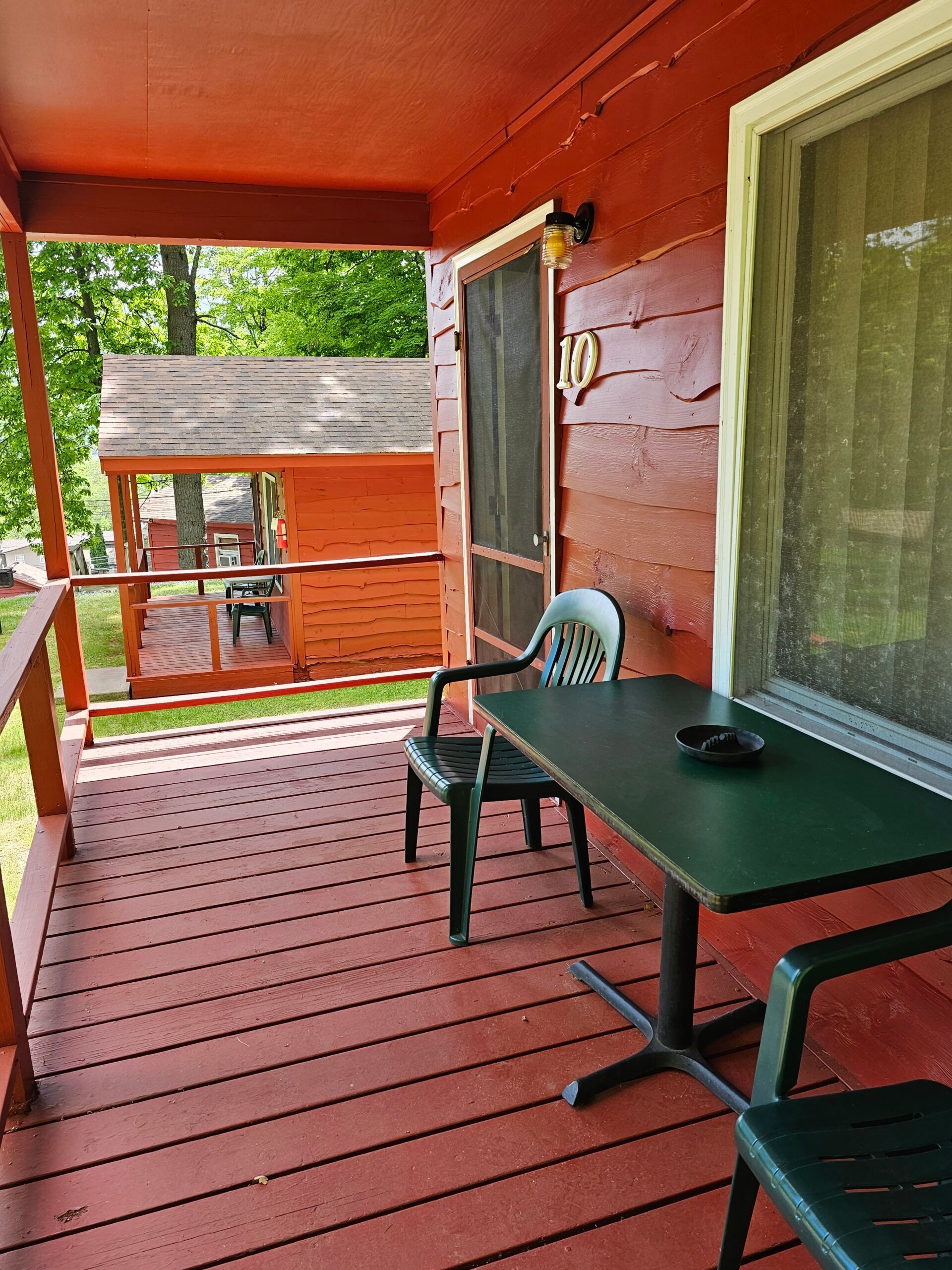 Red-painted porch with table and chairs overlooking a wooded yard
