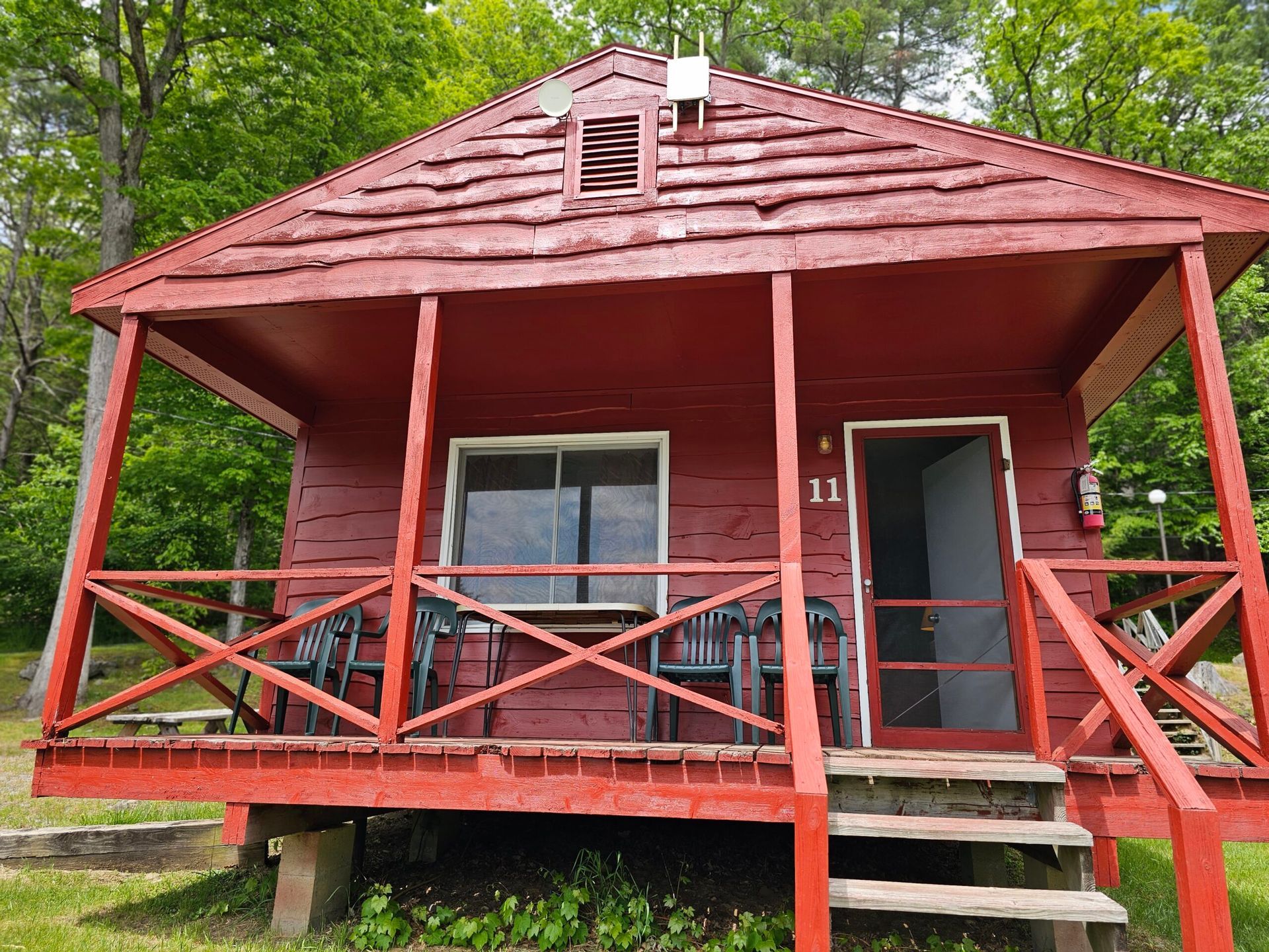Red wooden cabin with porch, steps, and front door in a wooded setting