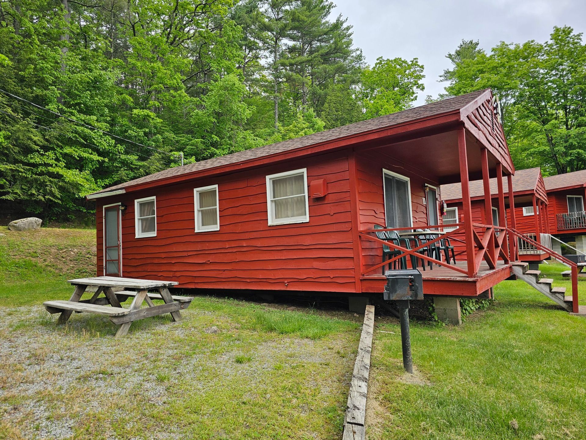 Red cabin with porch and picnic table in a wooded campsite