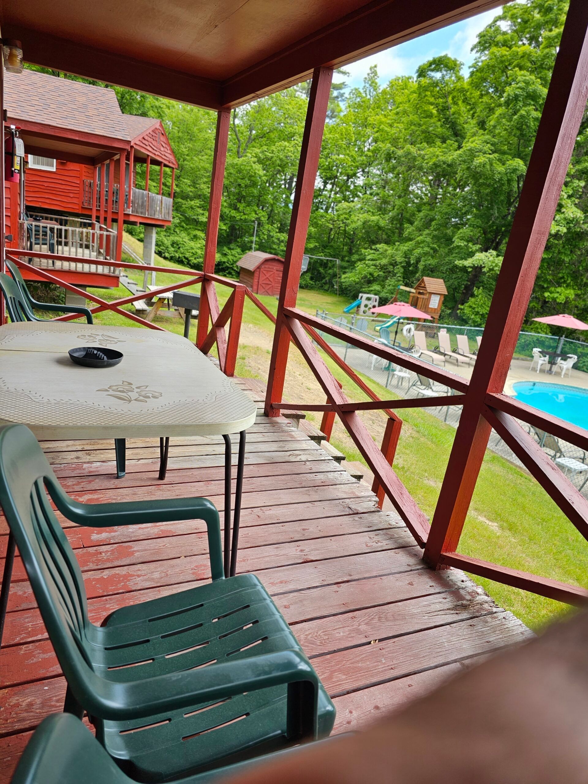Covered porch with green chairs and table overlooking a yard and blue swimming pool
