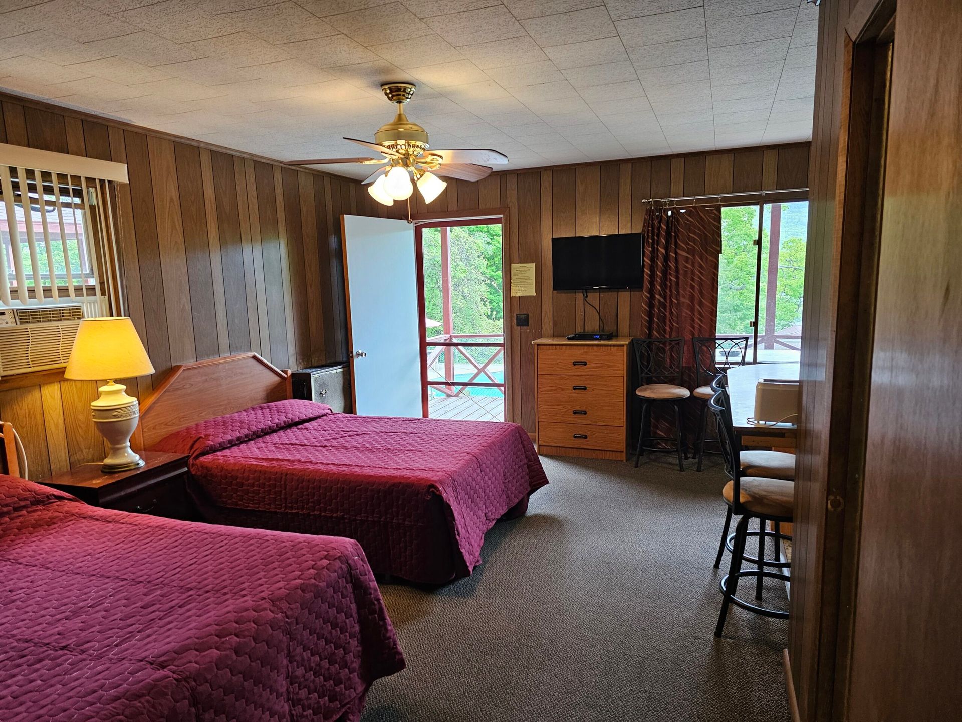 Motel room with two red beds, ceiling fan, TV, dresser, and patio door to a balcony