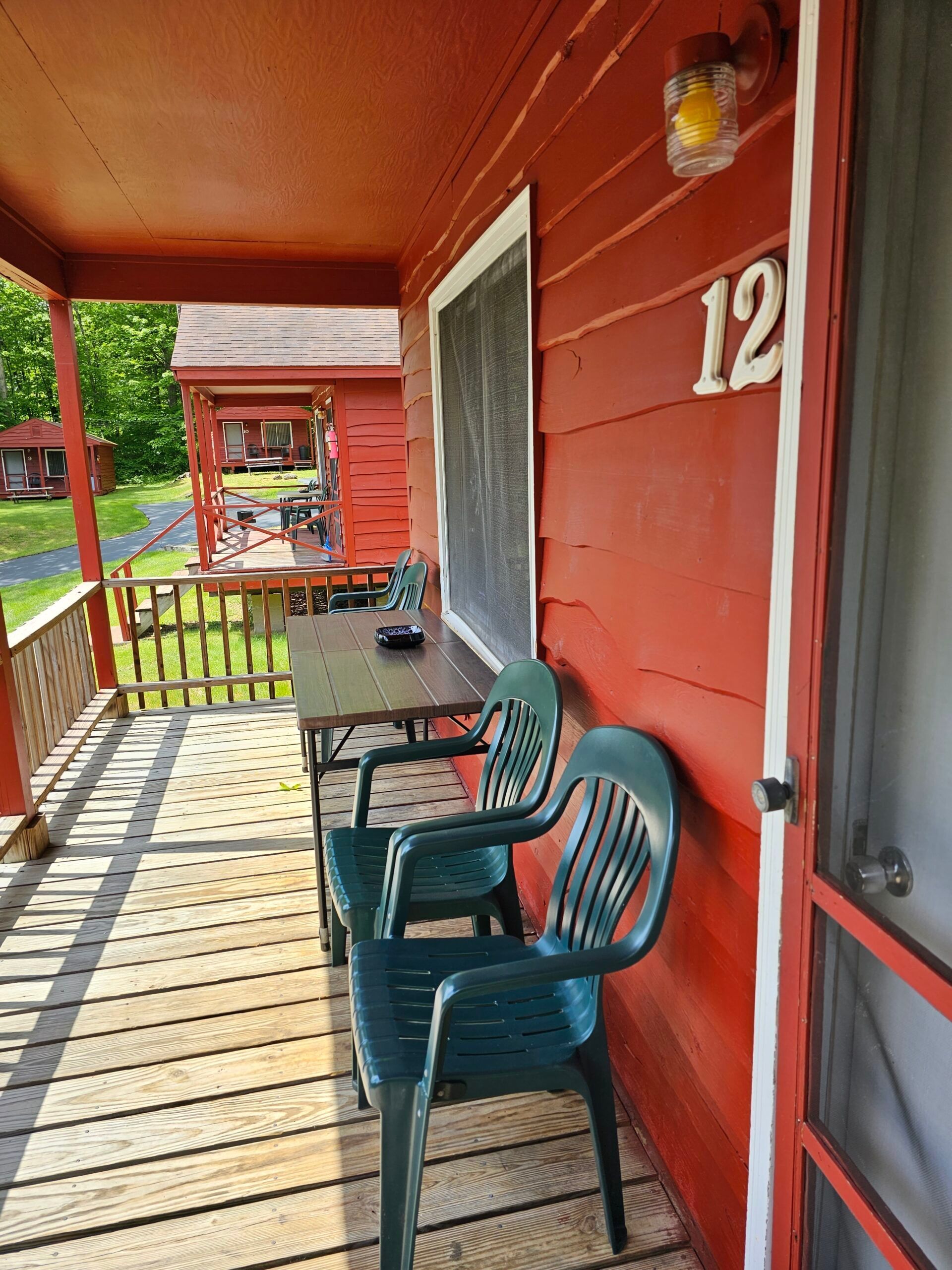 Red porch with two green chairs, a table, and house number 12 on the wall.