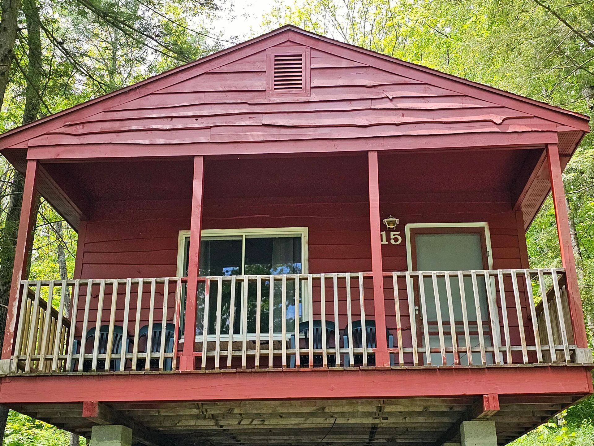Red wooden cabin porch with white railings and trees in the background