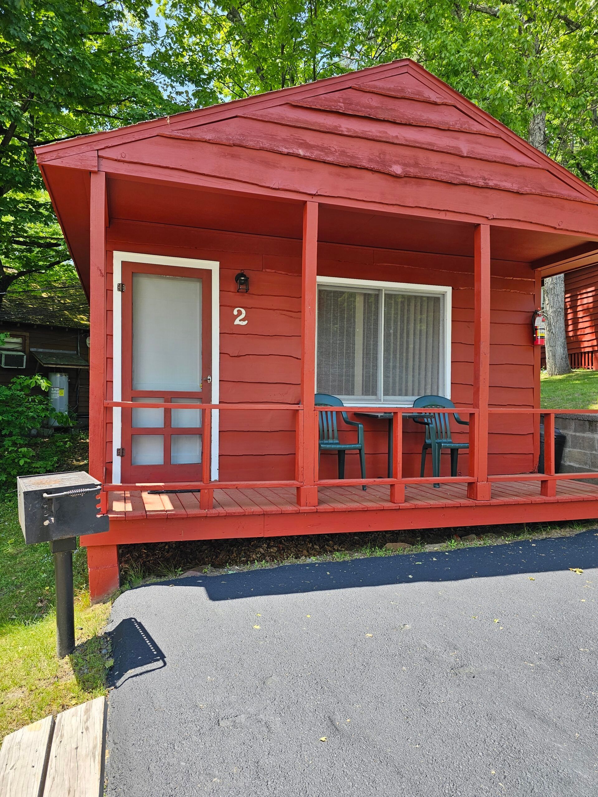 Red cabin porch with white trim, red railings, and a small table outside, surrounded by green trees.