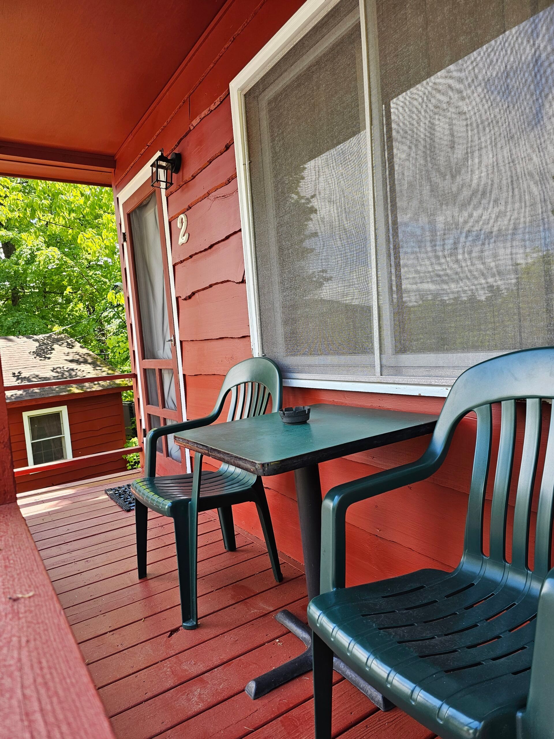 Red porch with two plastic chairs and a small table beside a screened window.