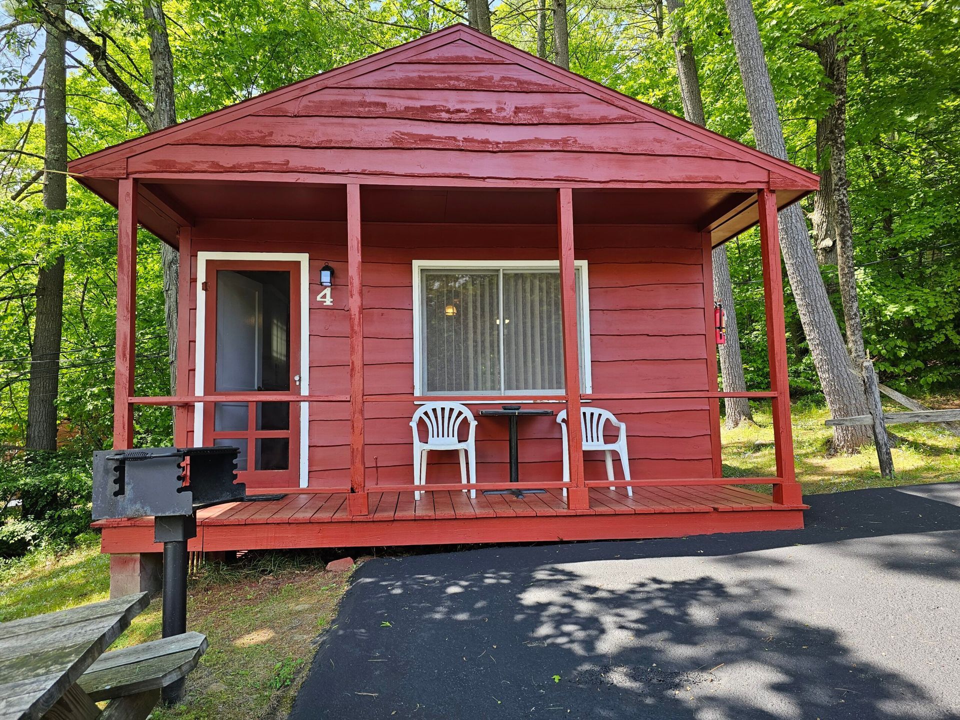 Red cabin with porch, white chairs, and a mailbox in a wooded park setting