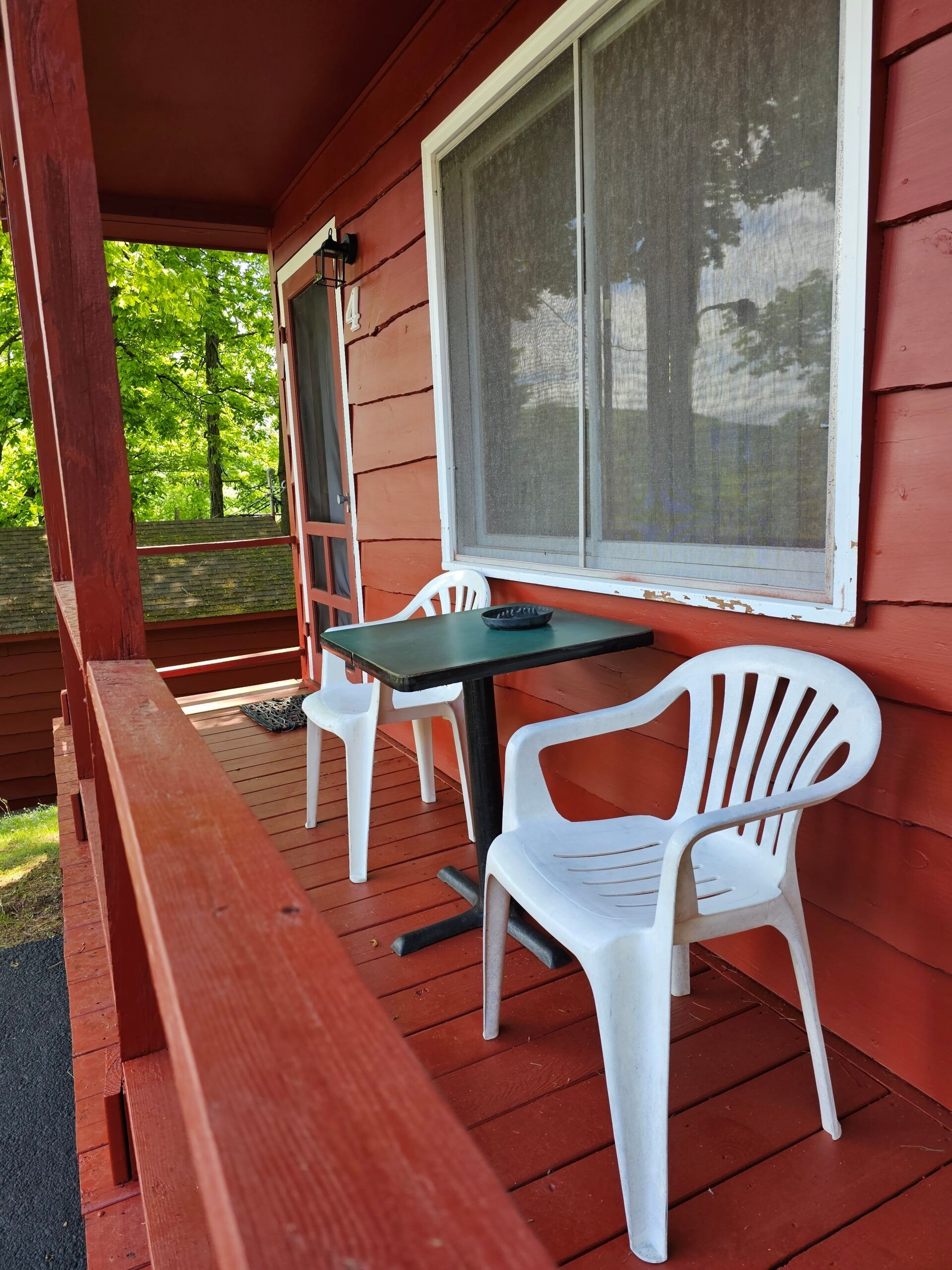 Red porch with two white chairs and a small table beside a screened window.