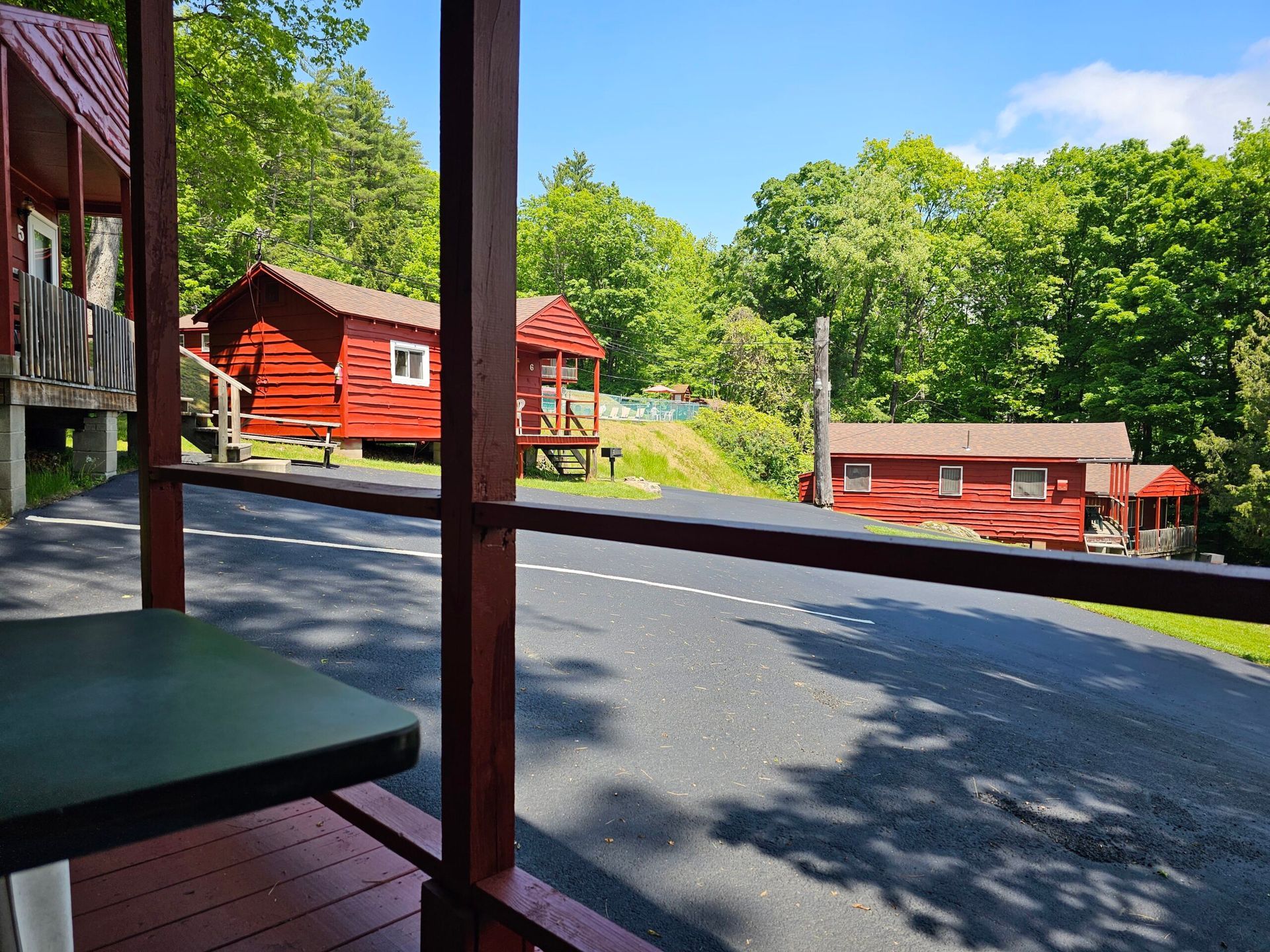 Red cabins and porches on a sunny wooded resort hillside, viewed from a shaded porch
