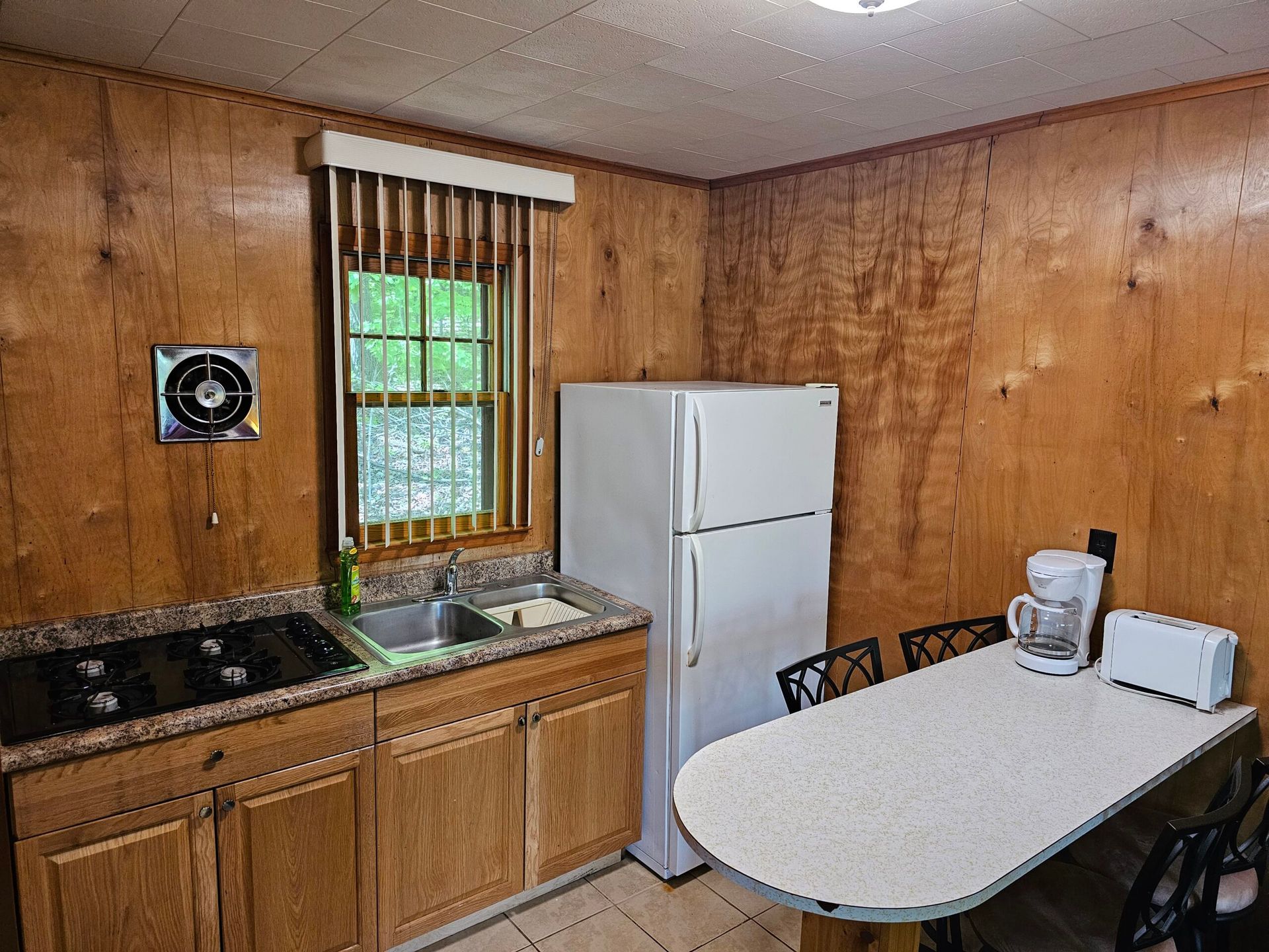 Small kitchen with wood-paneled walls, white fridge, sink, stove, and a table with a blender and toaster.