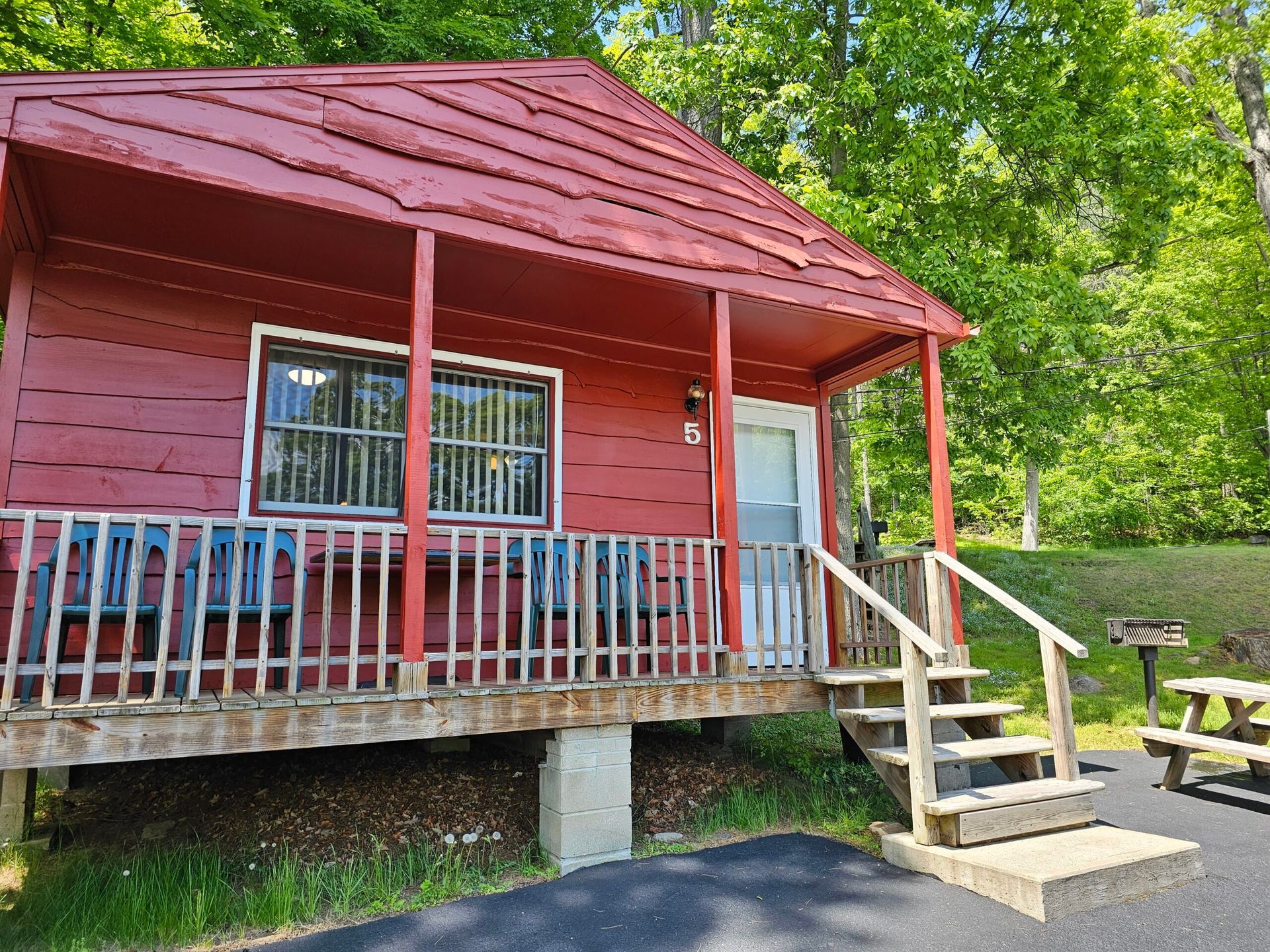 Small red cabin with porch, steps, and railings nestled among green trees.