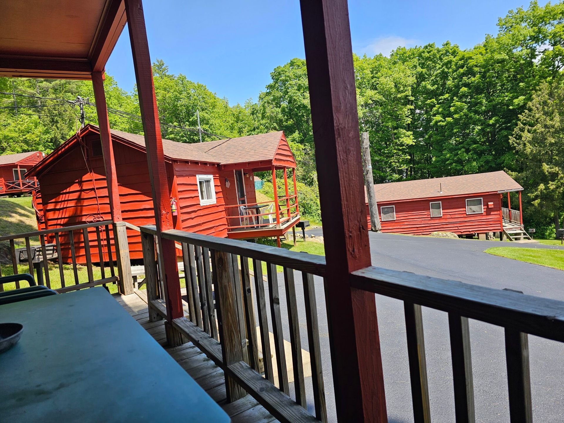 Cabin porch overlooking red log cabins and a forested campground on a sunny day