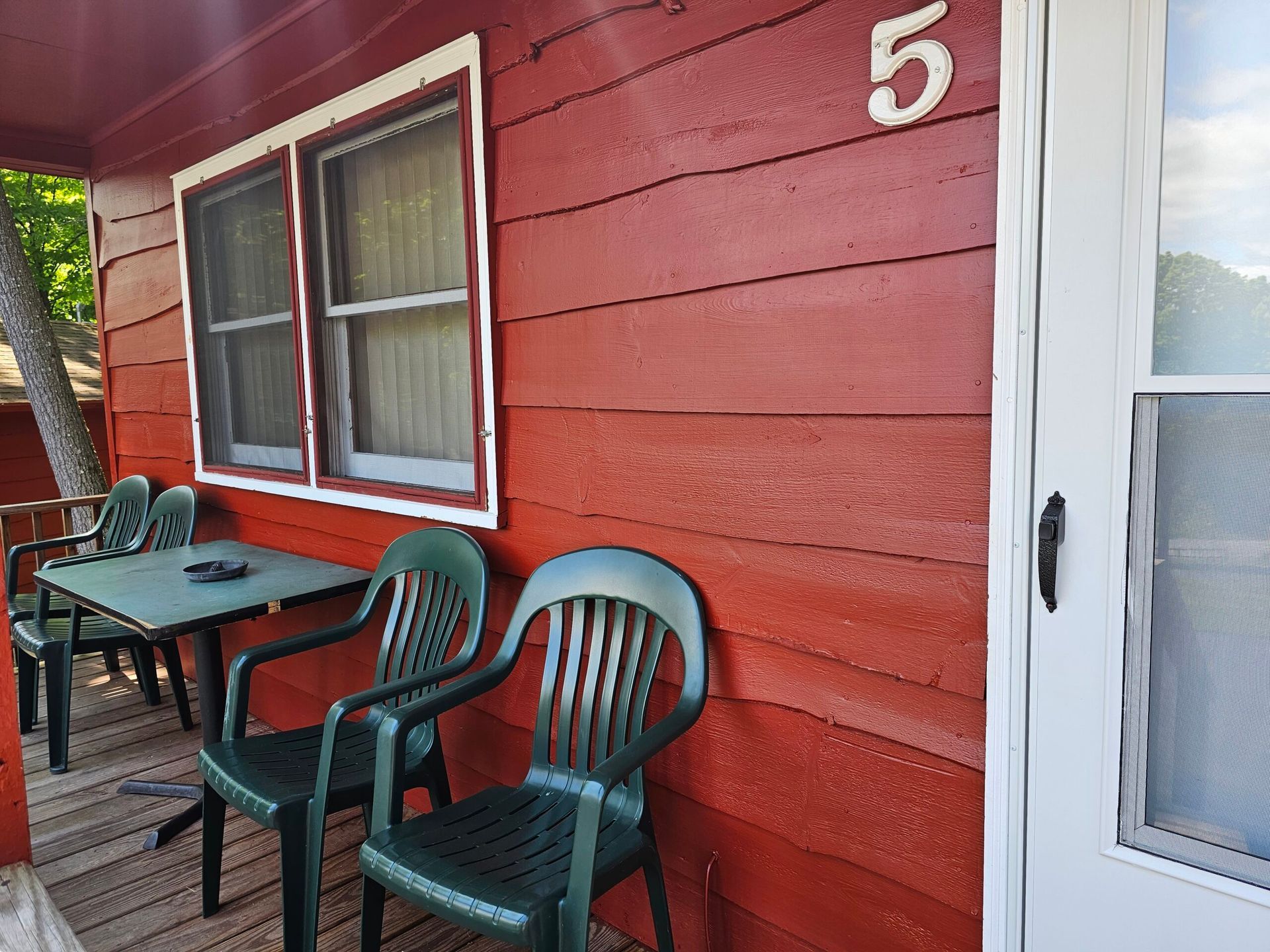 Red cabin porch with table, chairs, and white door; number 5 above the entrance.