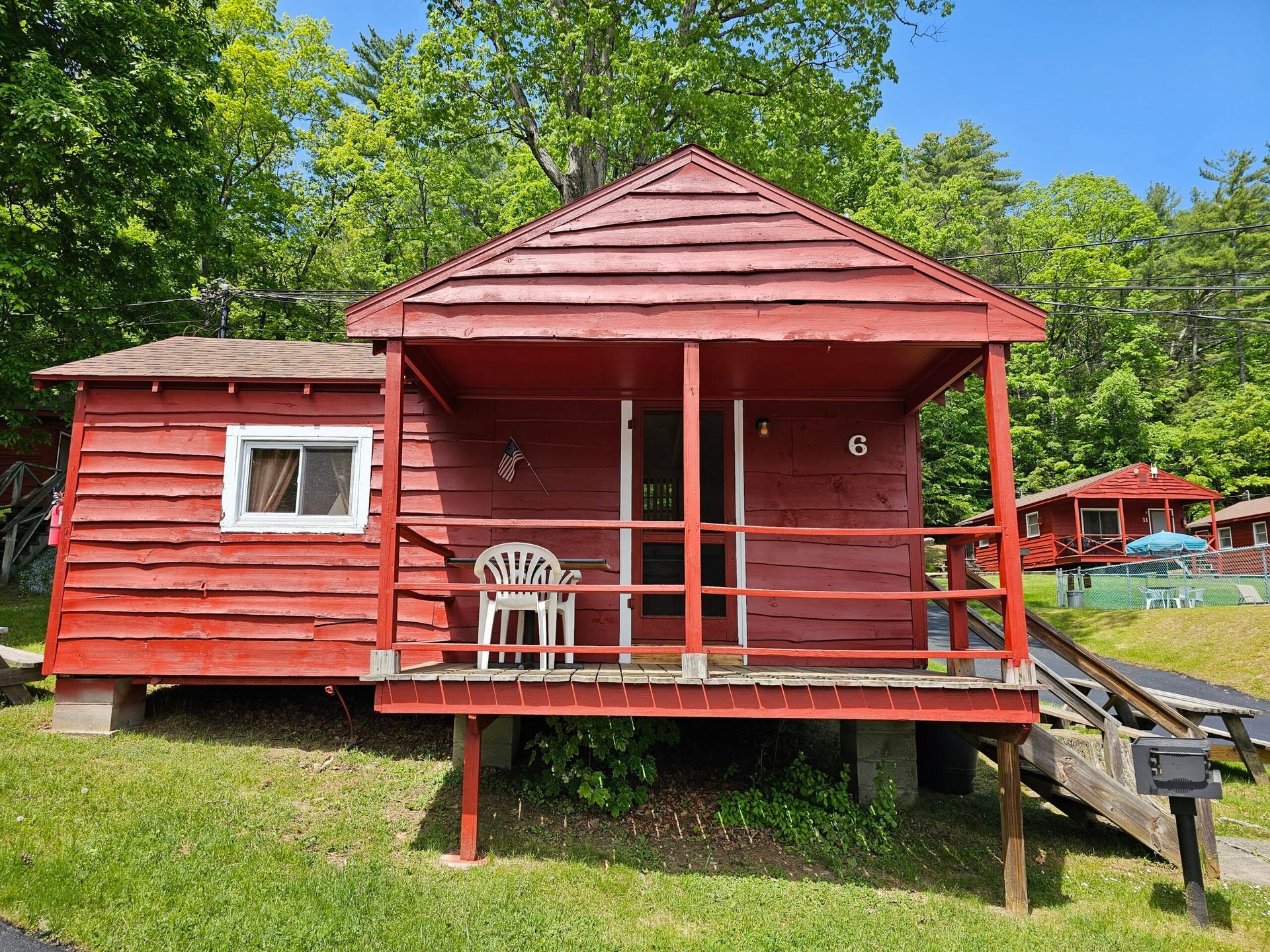 Red cabin with porch and white chair in a grassy wooded campsite