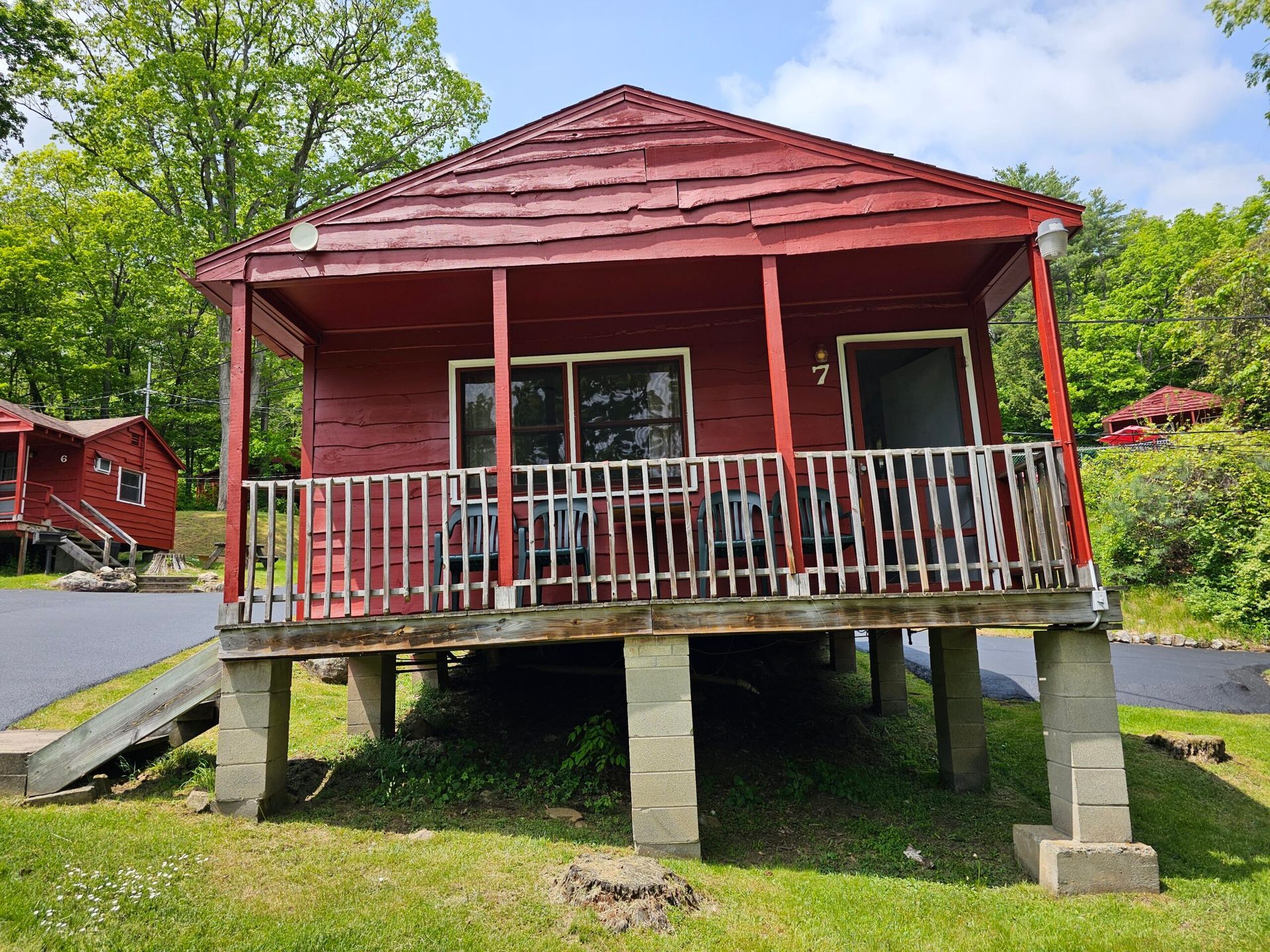 Red cabin with a front porch, red roof, and steps, set in a green wooded area.