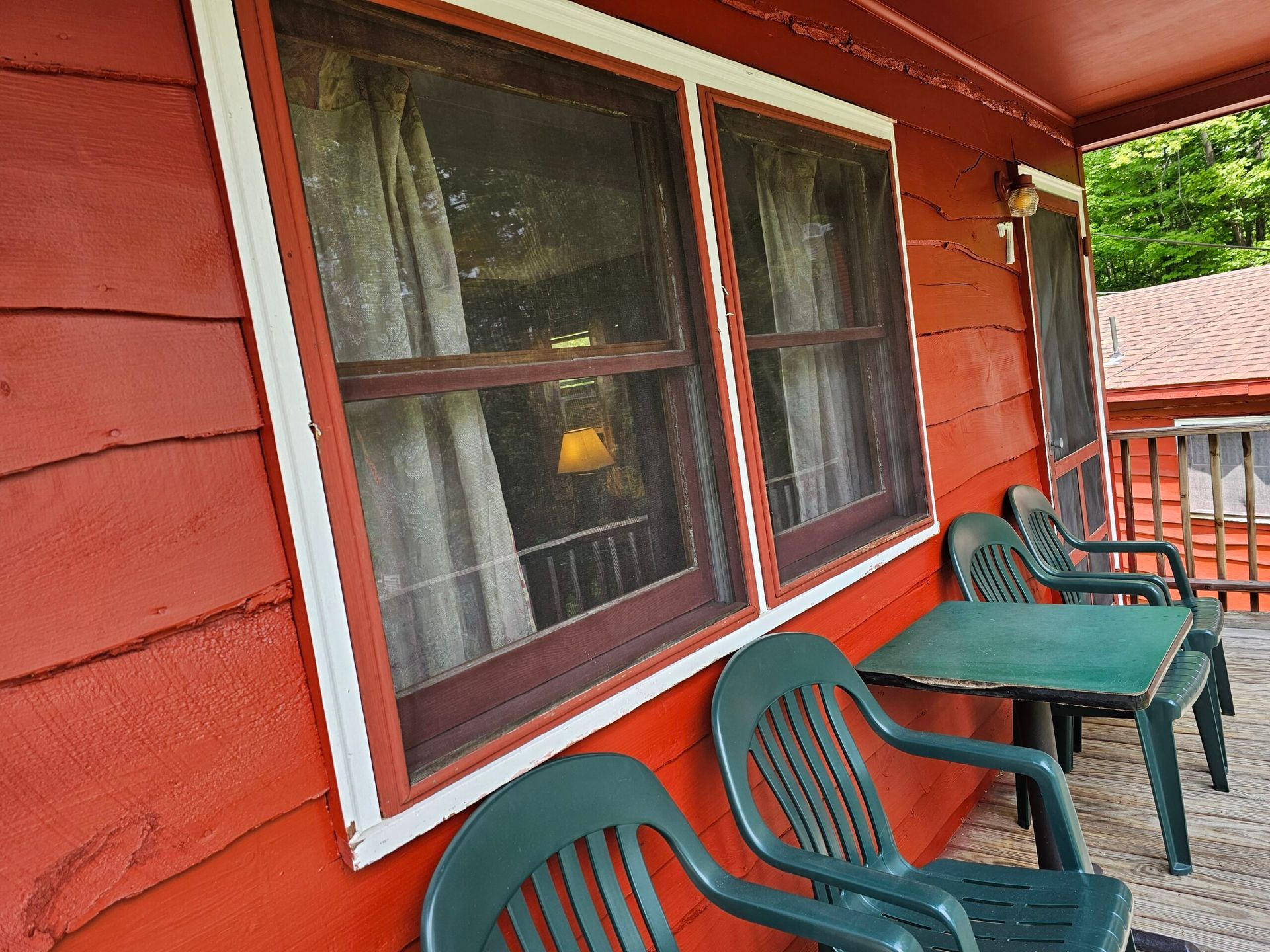 Red cabin porch with white-trimmed windows, green chairs, and tables along the wall.