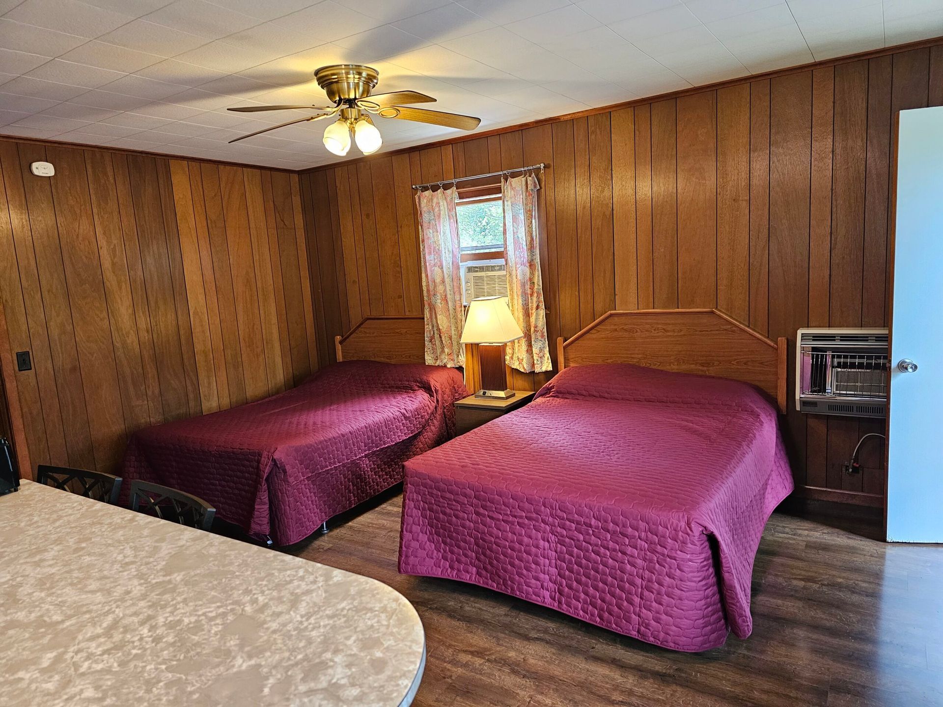Motel room with two beds, wood-paneled walls, ceiling fan, and bedside lamp.