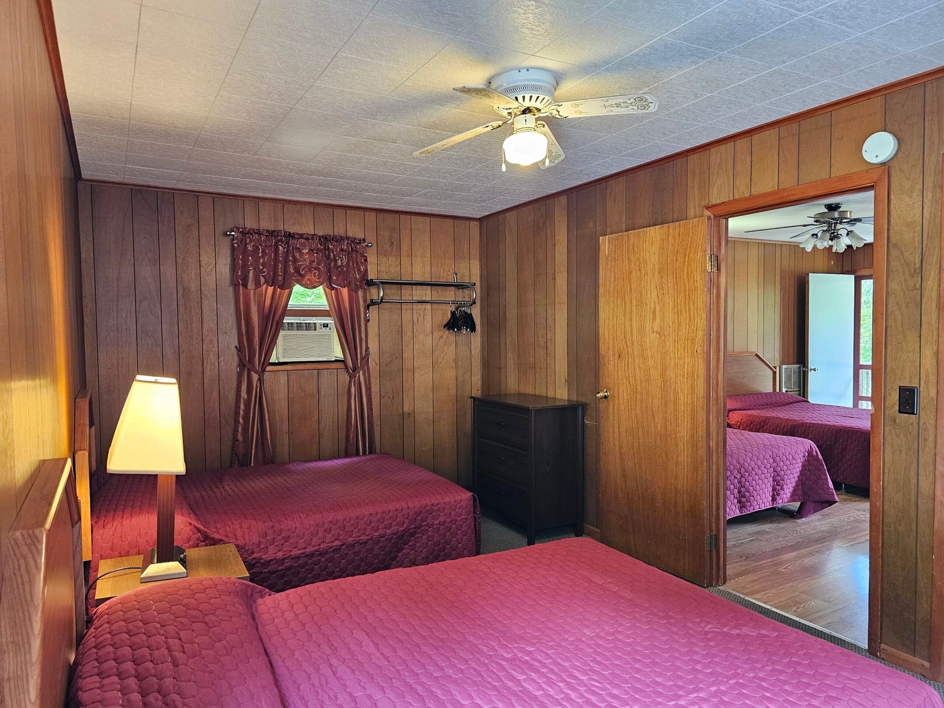 Wood-paneled bedroom with two beds, lamp, ceiling fan, and mirrored closet door