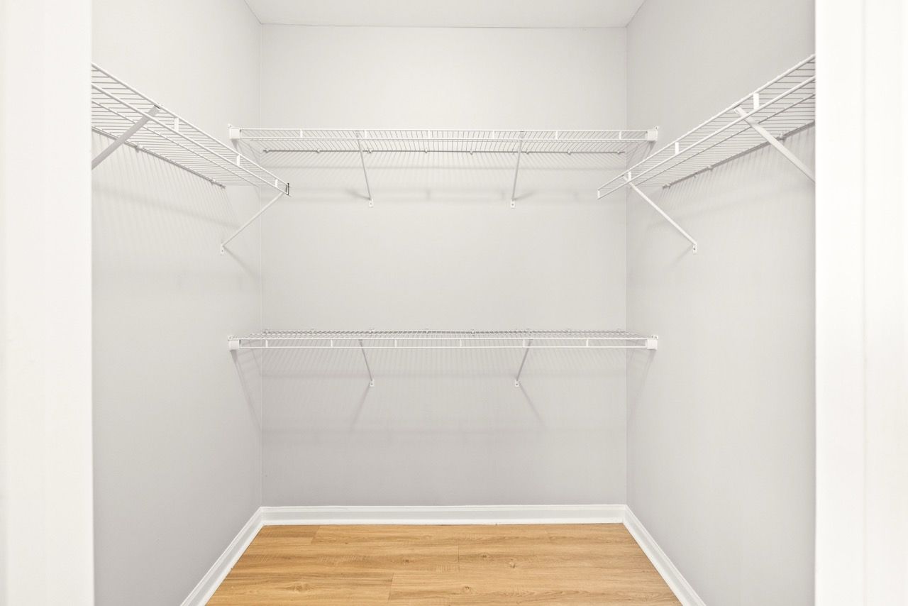 Empty walk-in closet with white wire shelves and light wood floor.