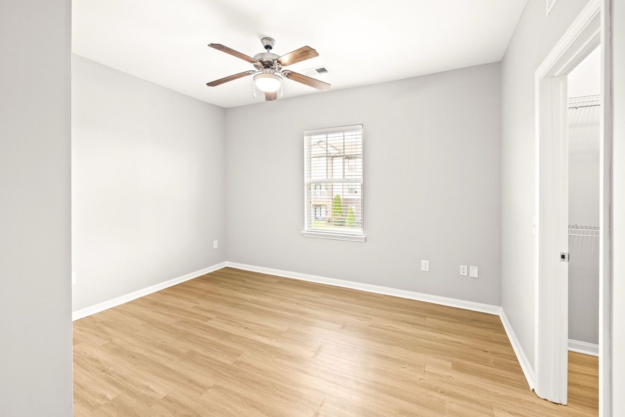 Empty bedroom with gray walls, wood flooring, window, ceiling fan, and closet.
