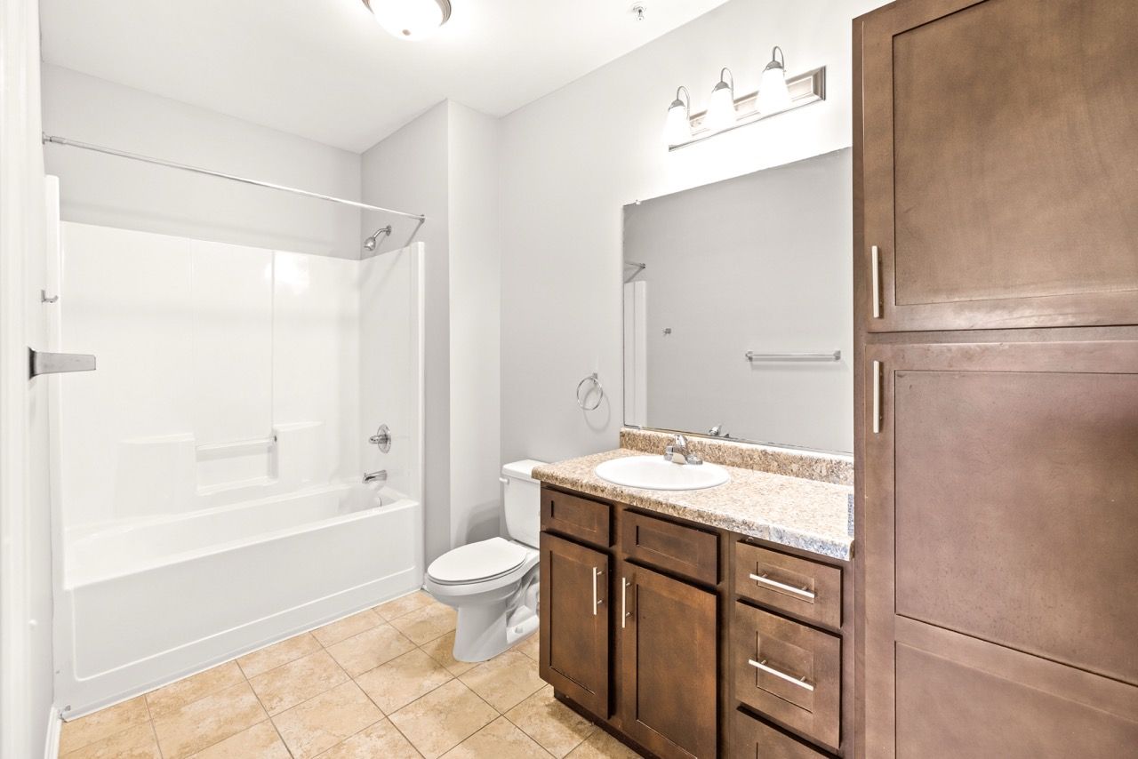 Bathroom with granite countertop vanity, dark wood cabinets, toilet, and white bathtub/shower.