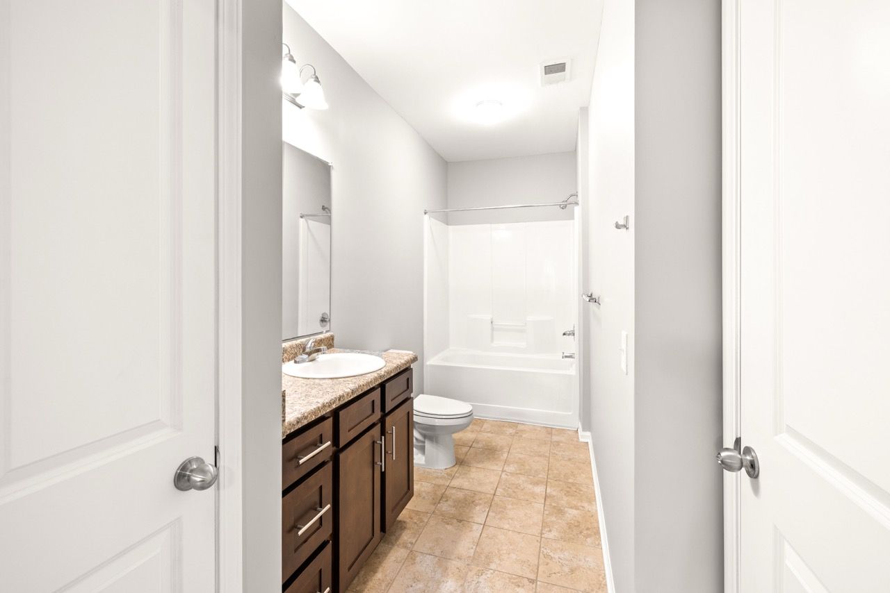 Bathroom in an apartment with a granite vanity, sink, toilet, and tub/shower.