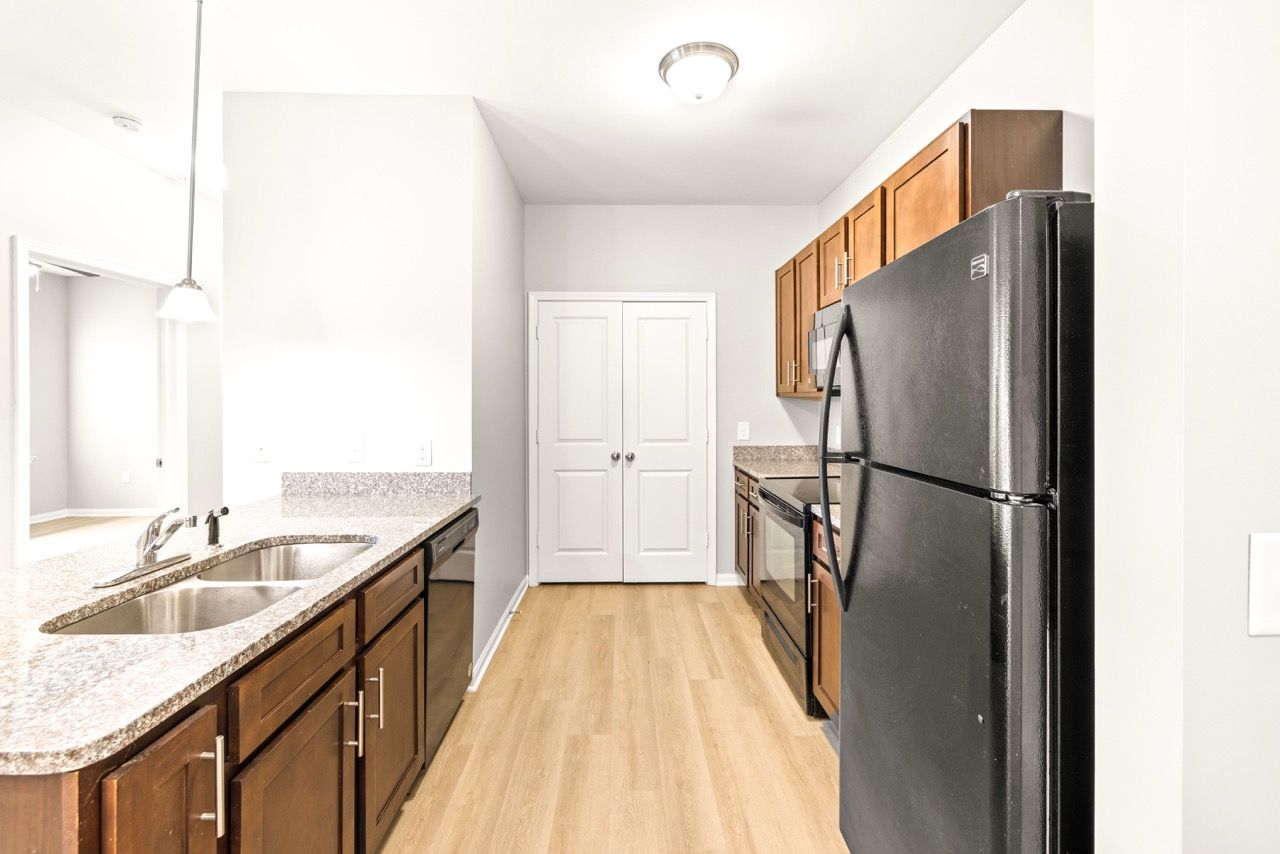 Modern apartment kitchen with granite countertops, double sink, wooden cabinets, and a black refrigerator.